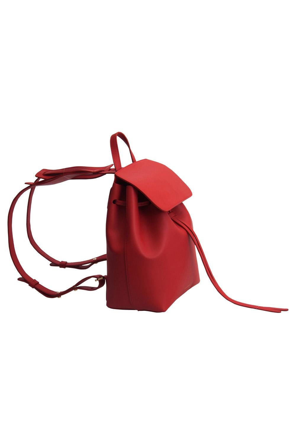 This stylish backpack from Mansur Gavriel is crafted from red leather and enhanced with gold-tone hardware. The bag features a top handle and adjustable shoulder straps. A flap secures the drawstring closure that opens to reveal a spacious
