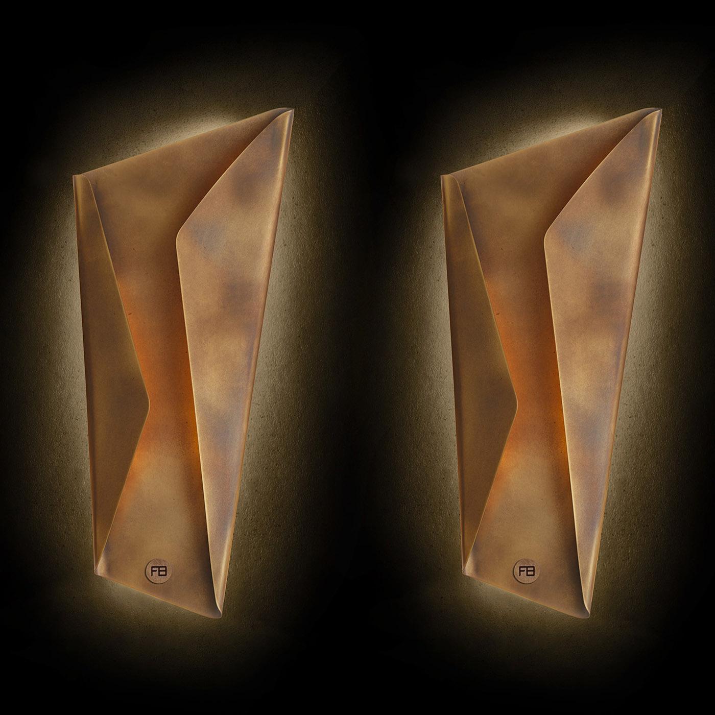 Wall lamp designed in two configurations and two different sizes, composed of curved laser-cut metal sheets available in different finishes: burnished brass, bronze, and graphite. It can be installed both horizontally and vertically. Double ignition