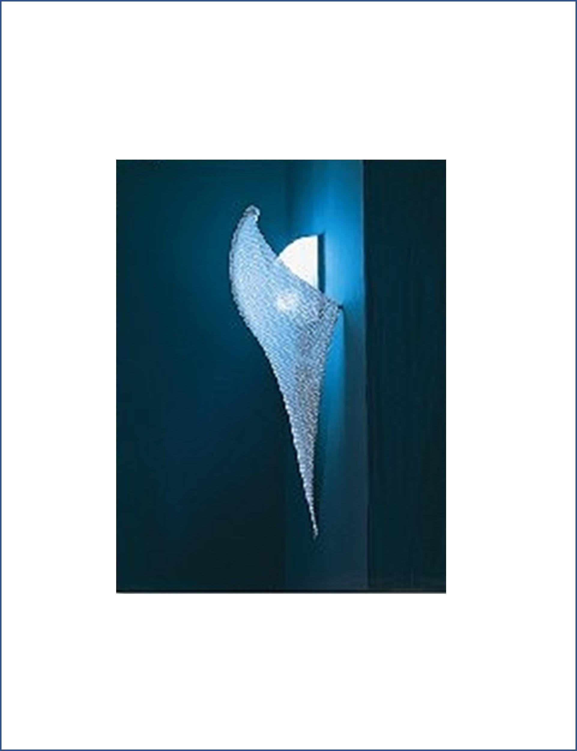 The graceful shape of the giant Manta Ray inspired this wall sconce. A chain mail diffuser stretches over a central curved spine and is pinned on both sides and at the bottom to give it its sculptural shape. Manta was featured in numerous magazines