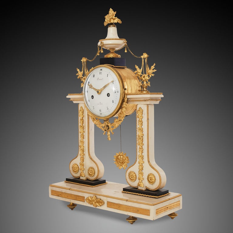 This elegant portico clock crafted in transitional Louis XVI – Empire style from ormolu, white and black marble, is signed on the dial “Arnoux à Paris”. Decorative motifs of Louis XVI style were inspired by nature and antiquity with characteristic