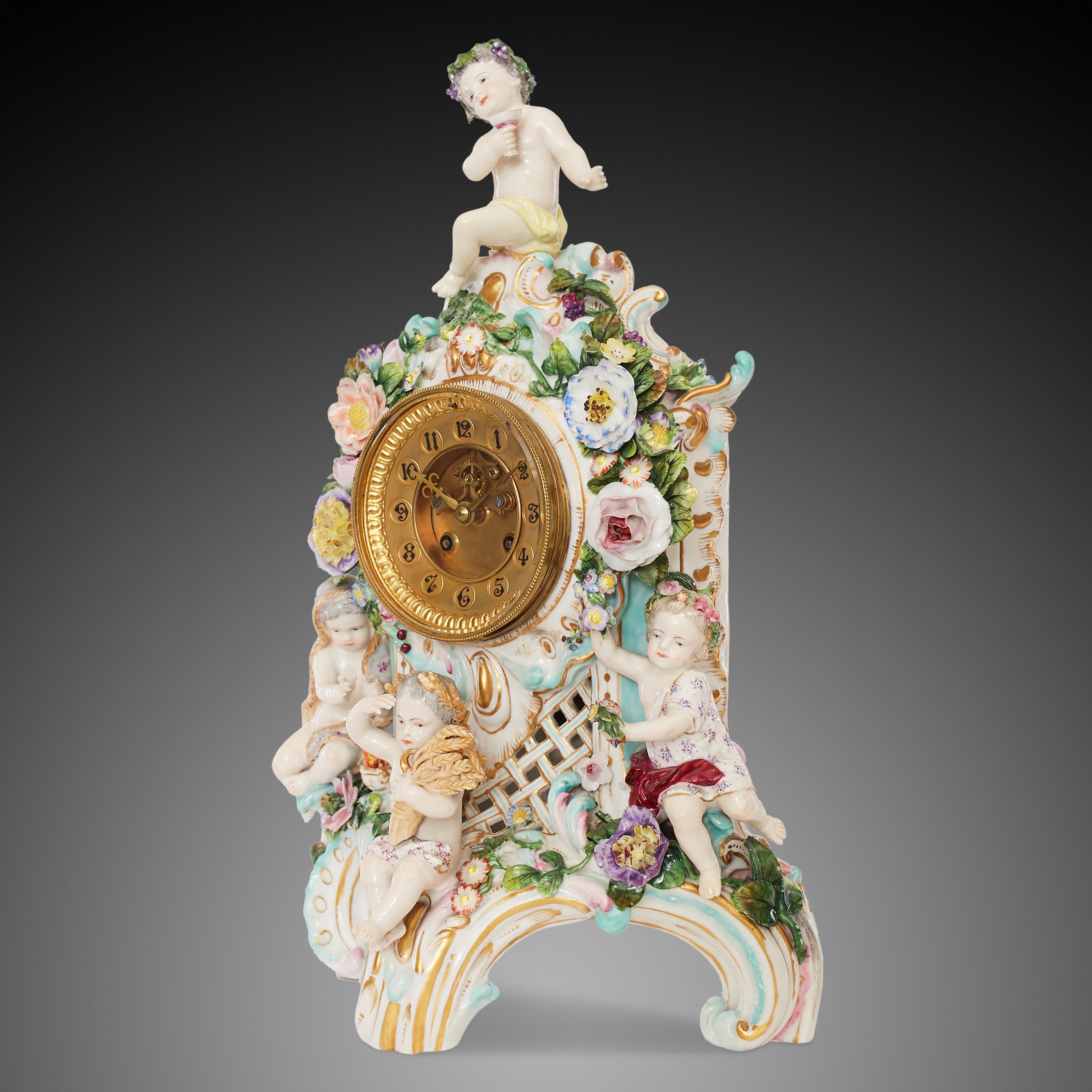 This 19th-century German Rococo style porcelain clock is decorated with colourful figures and flowers.
The clock features four putti, each one represents a different season. Summer is represented by the surmounting putto, shown holding a chalice