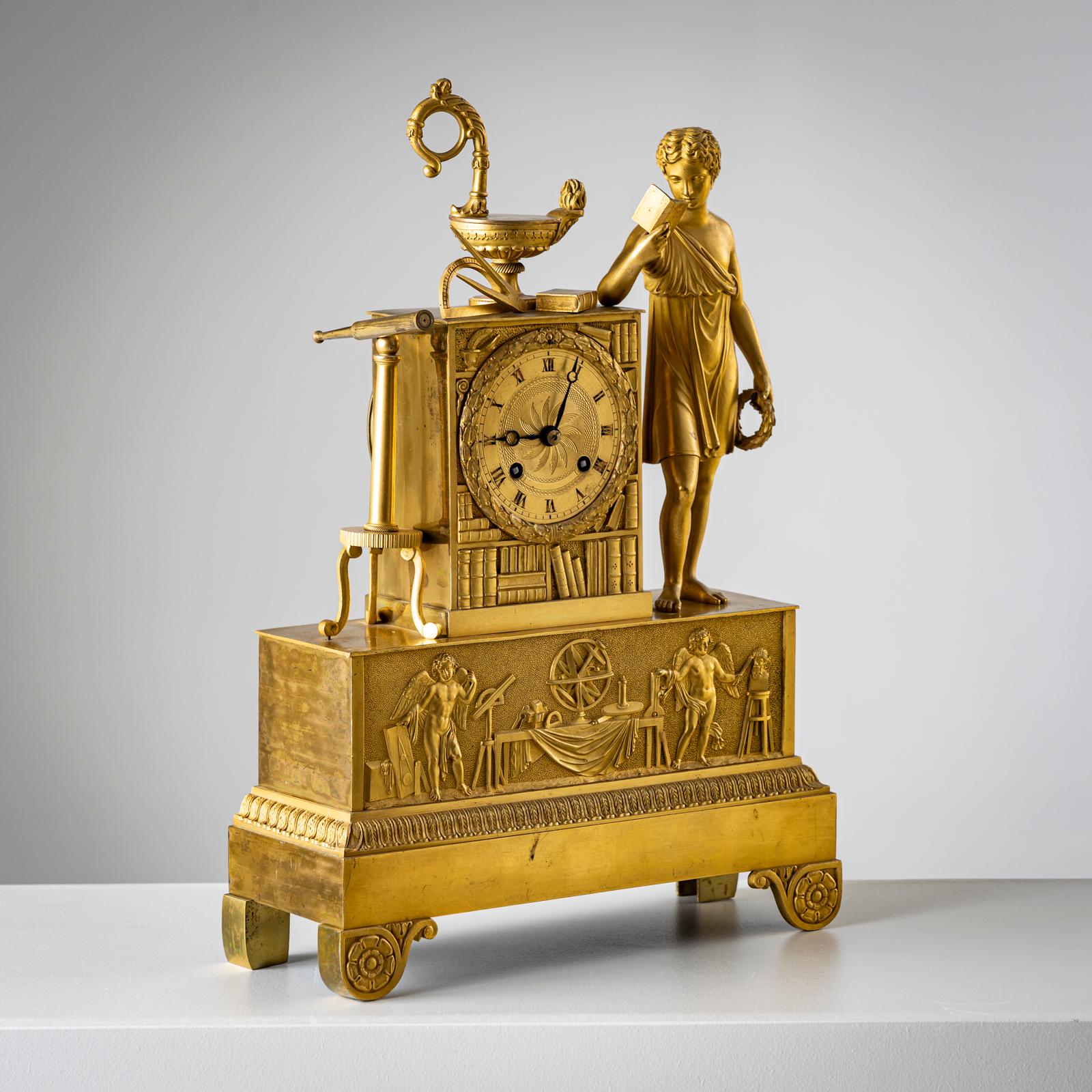Fireplace clock made of fire-gilt bronze with a rectangular base with a relief depicting winged putti with the attributes of the various sciences. Above it is a clock case in the shape of a bookshelf with a young man reading at the side as well as
