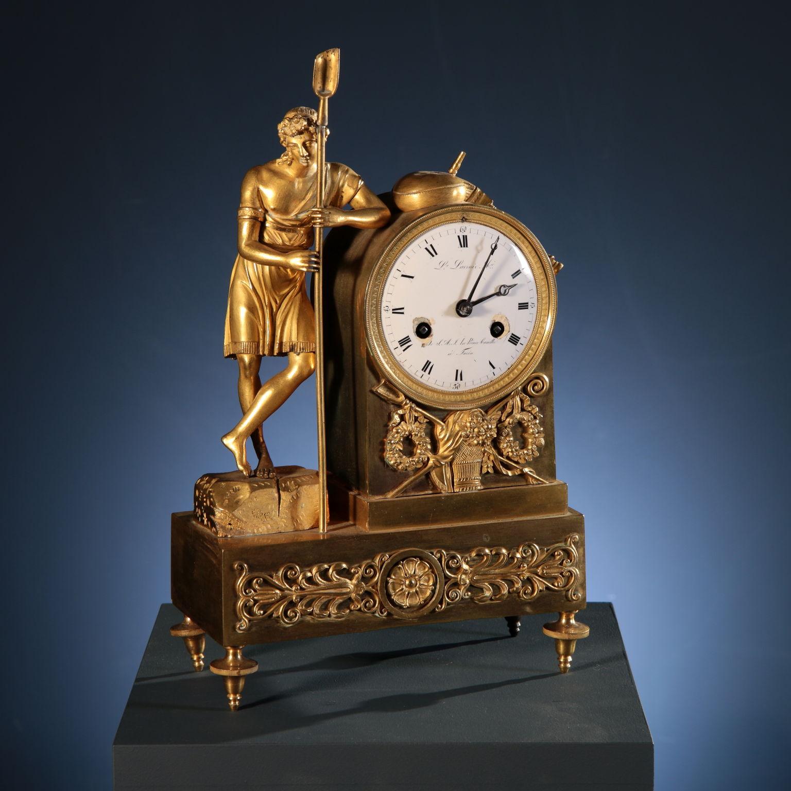 The gilt bronze mantel clock has a base decorated on the front with leafy phytomorphic motifs and a central floral element, and is supported by elaborate spinning top feet that streamline its shape. On the base rests a large plinth in which the dial