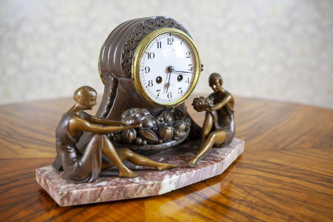 Mantel Clock With Marble Base From the Turn of the Centuries

The case with a hinged glass door, adorned with the figures of two seated women holding baskets of fruits, mounted on a marble base.
Mantel Clock in the Art Deco style