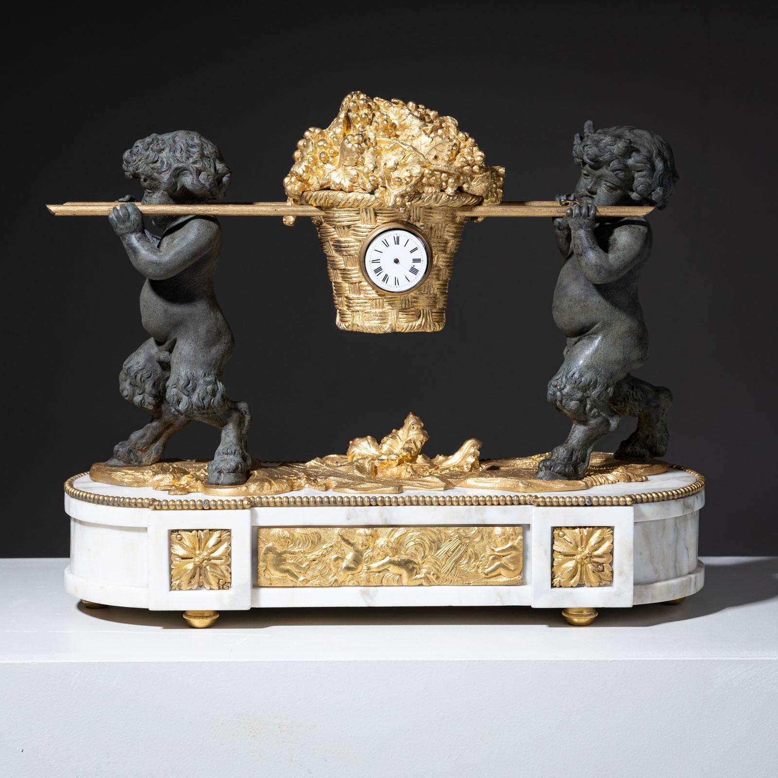 Mantel clock on an oval marble base, adorned with fire-gilded bronze appliqués. The clock is supported by fully sculpted satyr figures carrying an overflowing gilded fruit basket. Embedded in the basket is a small pocket watch mechanism, which