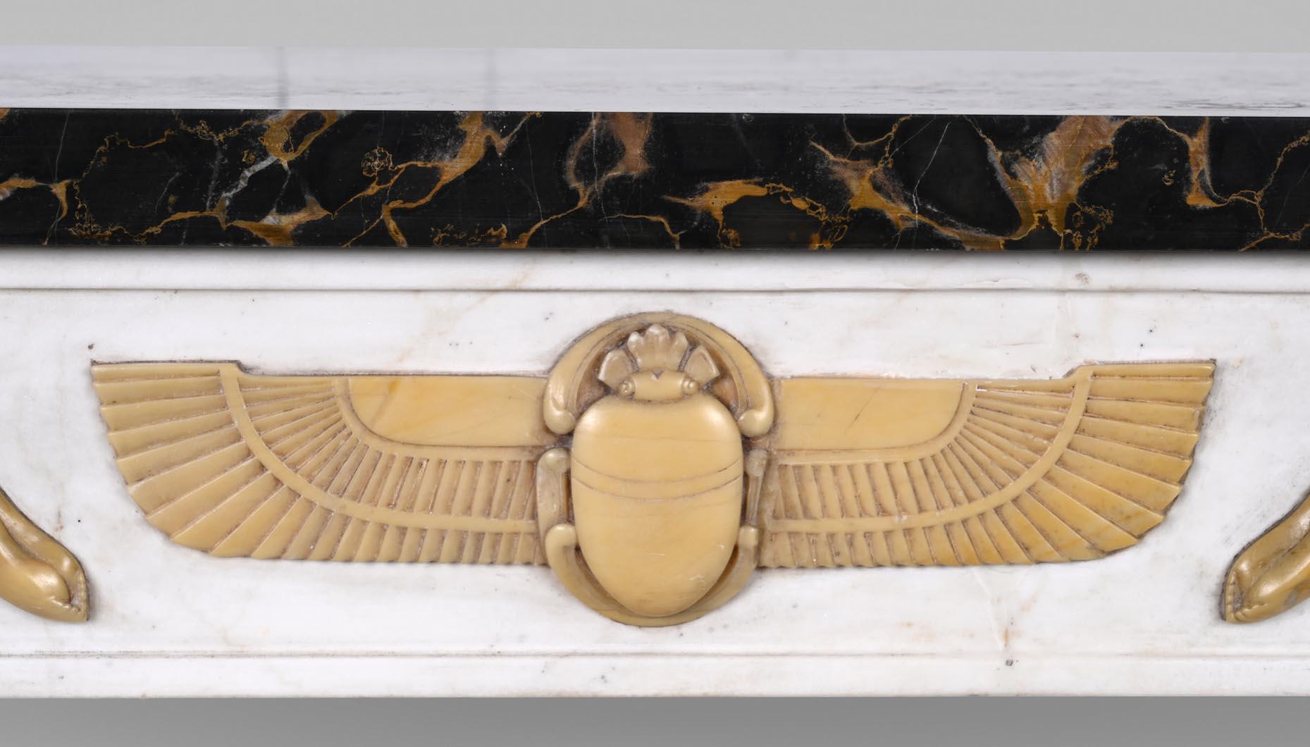 Cette cheminée ornée de décors d'inspiration égyptienne a été réalisée dans trois types de marbre vers 1830. Les bases et les chapiteaux des jambages, ainsi que le manteau, sont en marbre de Portoro, tandis que les jambages et le linteau sont en