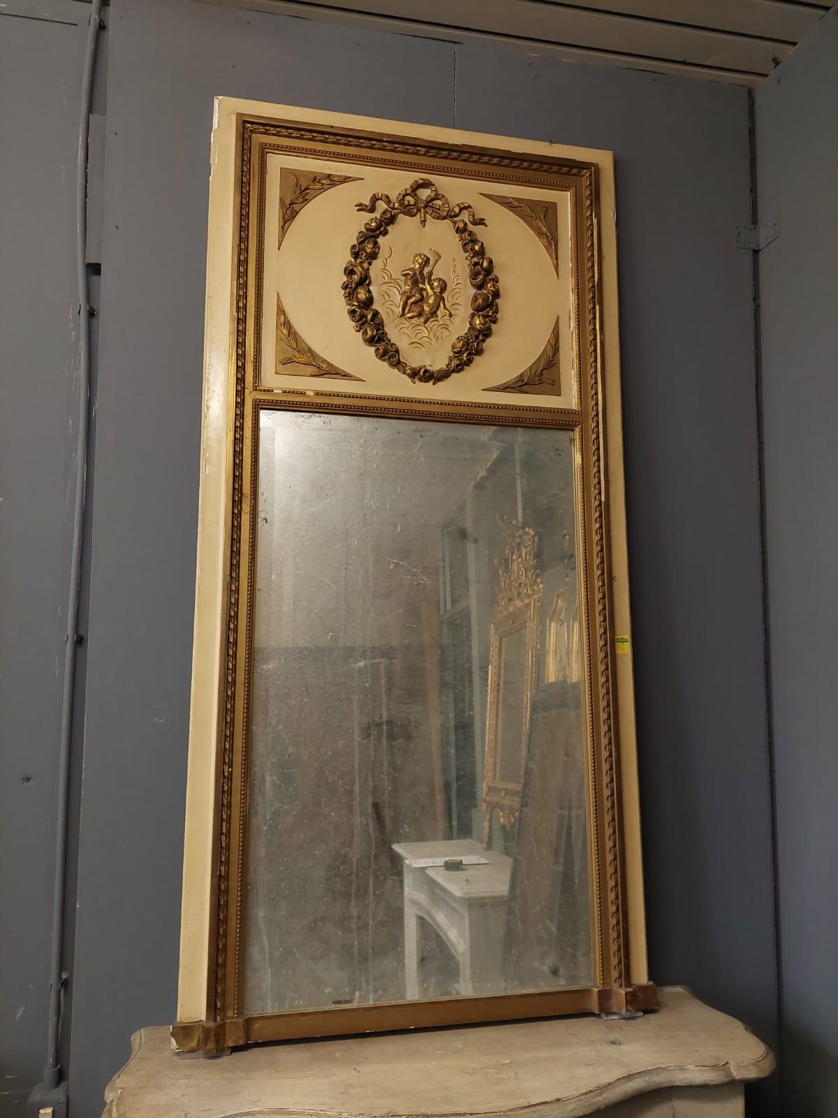 Antique fireplace or boiserie mirror, made of solid wood lacquered in opaque yellow, and carved with gilded wooden decorations, the upper part decorated with a garland that encloses two cherubs, original from the 19th century, from France, also