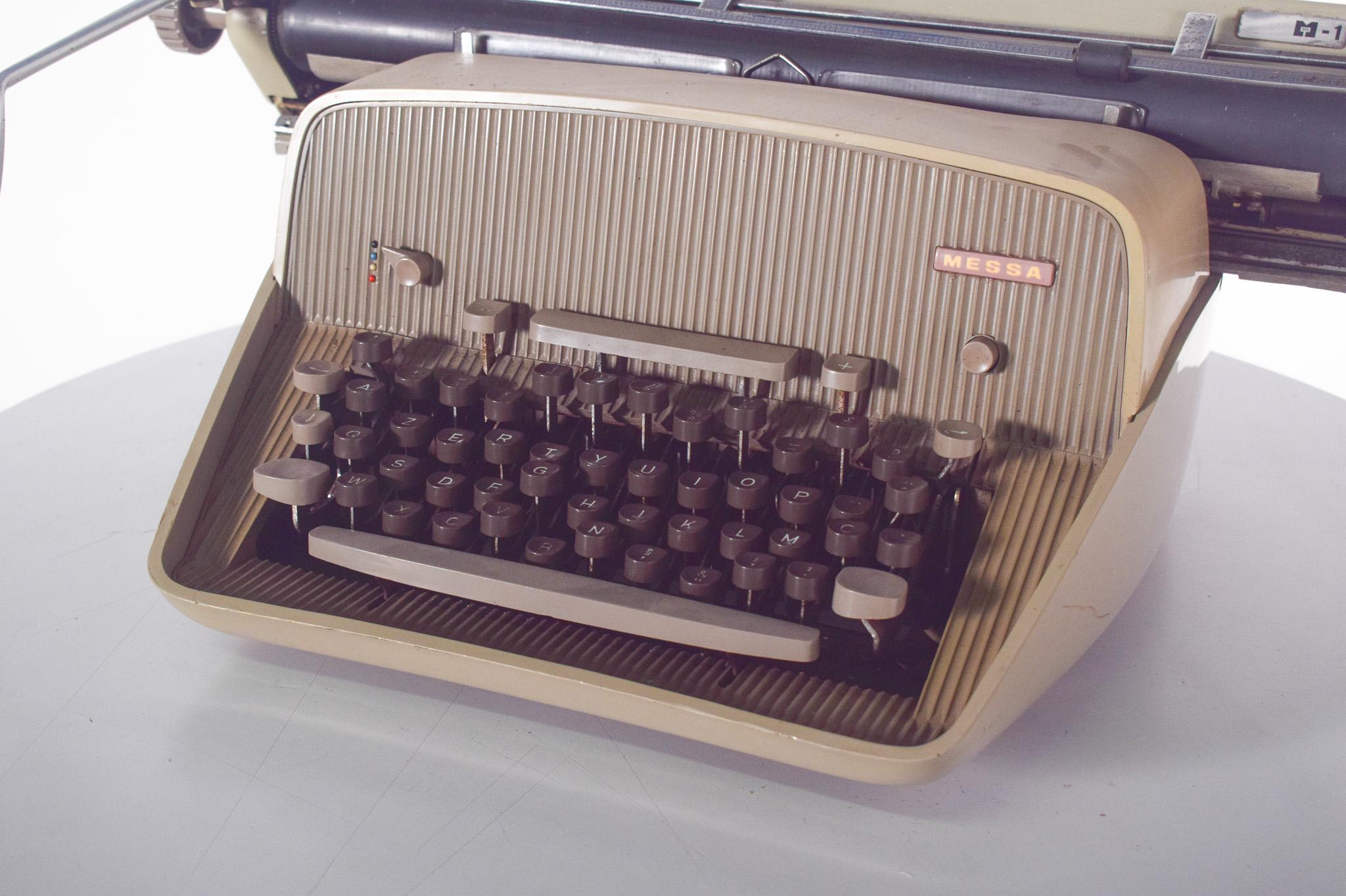 Handschreibmaschine, AZERTY-Tastatur von MESSA. Mit robustem Design, beiger Struktur und verchromten Metalldetails.
Die Tastatur weist die für klassische Schreibmaschinen typischen erhabenen, dunkel gefärbten runden Tasten auf, und der obere
