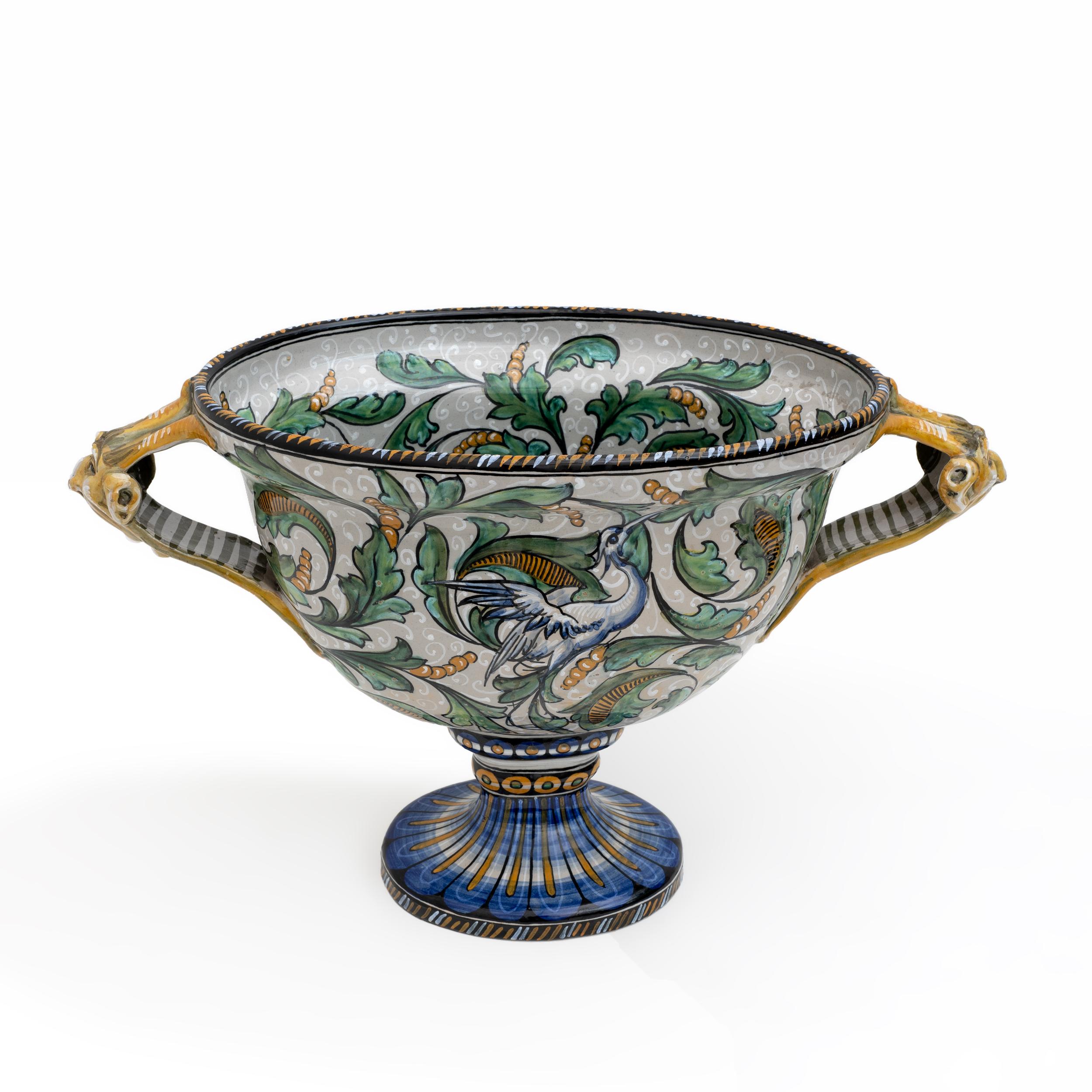 Tasse, Vase, zwei Henkel (mit zwei seitlichen Henkeln). Hergestellt in Pesaro, Italien, 1920.
Hergestellt aus mehrfarbiger künstlerischer Majolika, verziert mit Blättern und Vögeln.
Die beiden seitlichen Griffe sind mit Masken verziert.
Signiert am