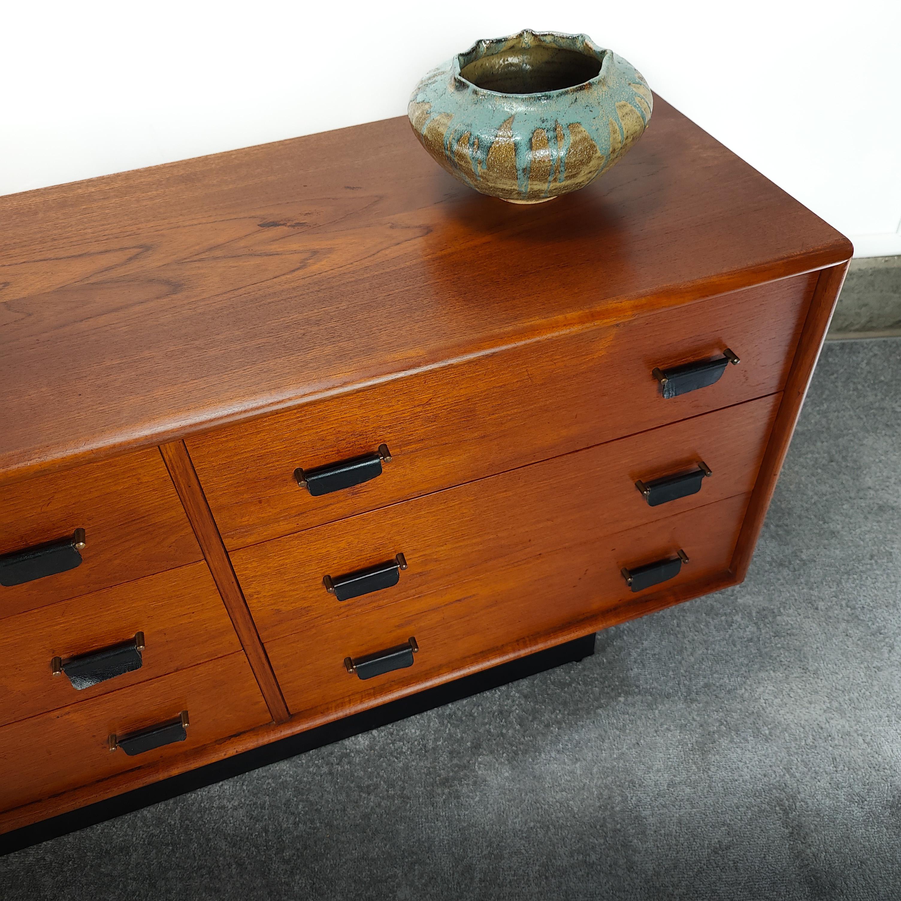 Striking 9 drawer pedestal plinth teak dresser by Intercontinental Design of Canada. Features brass hardware with leather pulls and base. Rich teak grain throughout. Measures approximately 76w x 18d x 27h. Stamped 