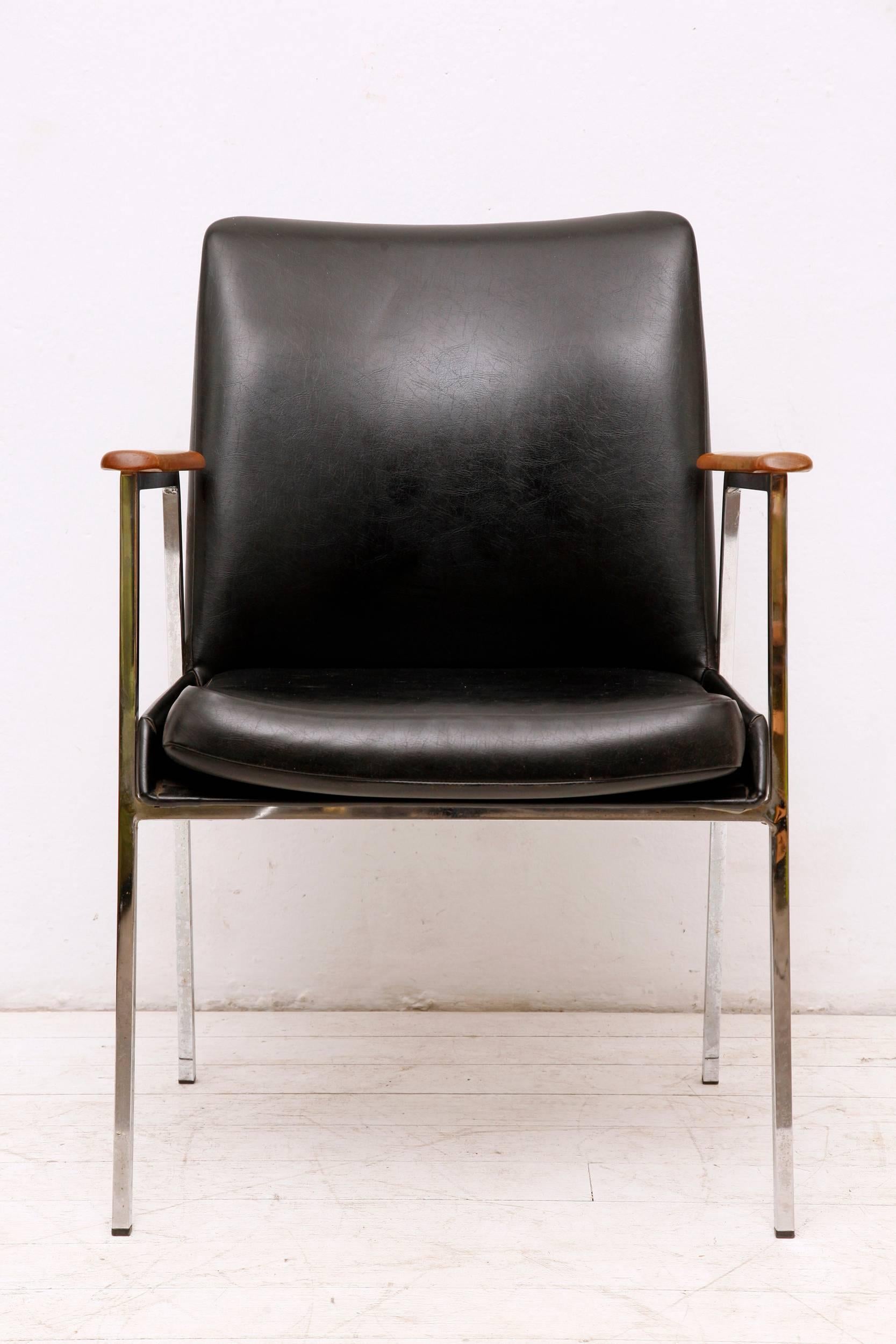 Mid-Century Modern (1960s) black armchair was manufactured by Mauser. The chair is in original condition. Seat and back are covered with dark faux leather, armrests are made of lacquered wood. The steel tube frame shows age-related