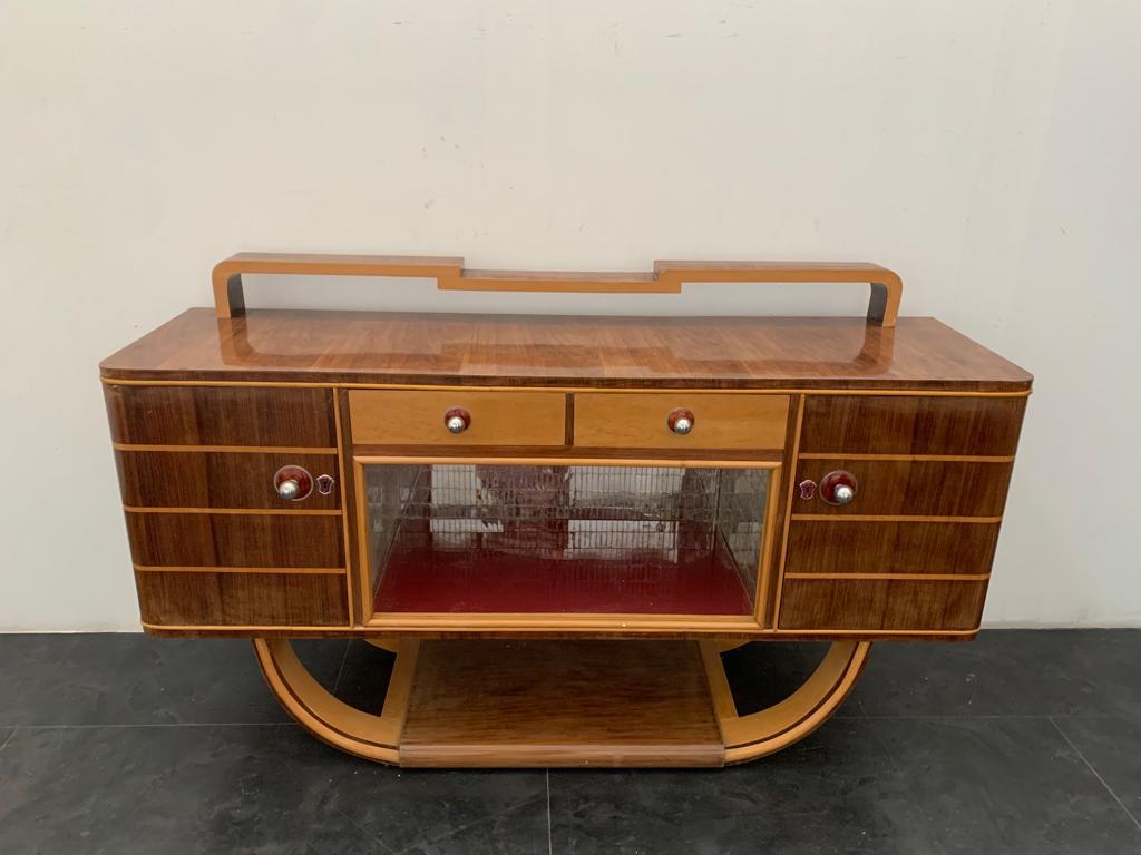 Art Deco sideboard with small riser made of plywood veneered in walnut and maple. The open compartment is characterised by a mirror mosaic resting on red glass, sliding glass doors missing. Details in chrome and red. Light darkening on the polish