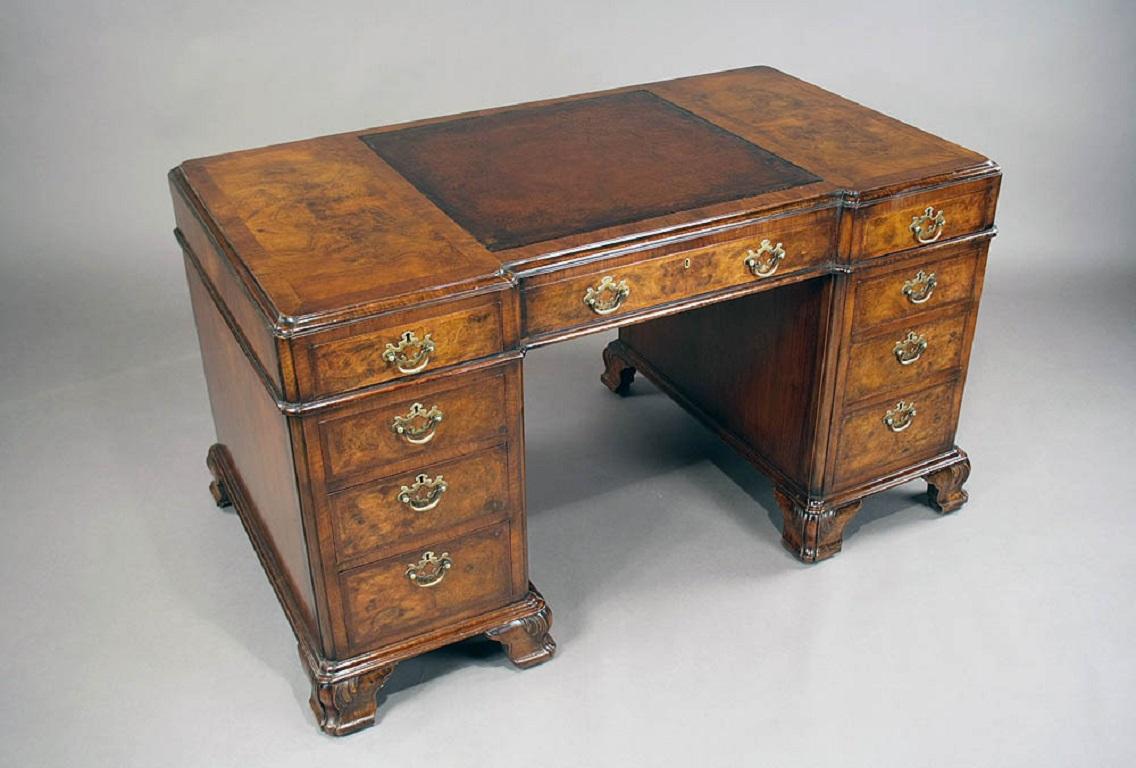 A fine quality burl walnut pedestal desk with inset leather top dating from the early 1900s. This fine quality walnut desk has an inverted molded breakfront top with two crossbanded burl walnut panels flanking a central original leather insert. The
