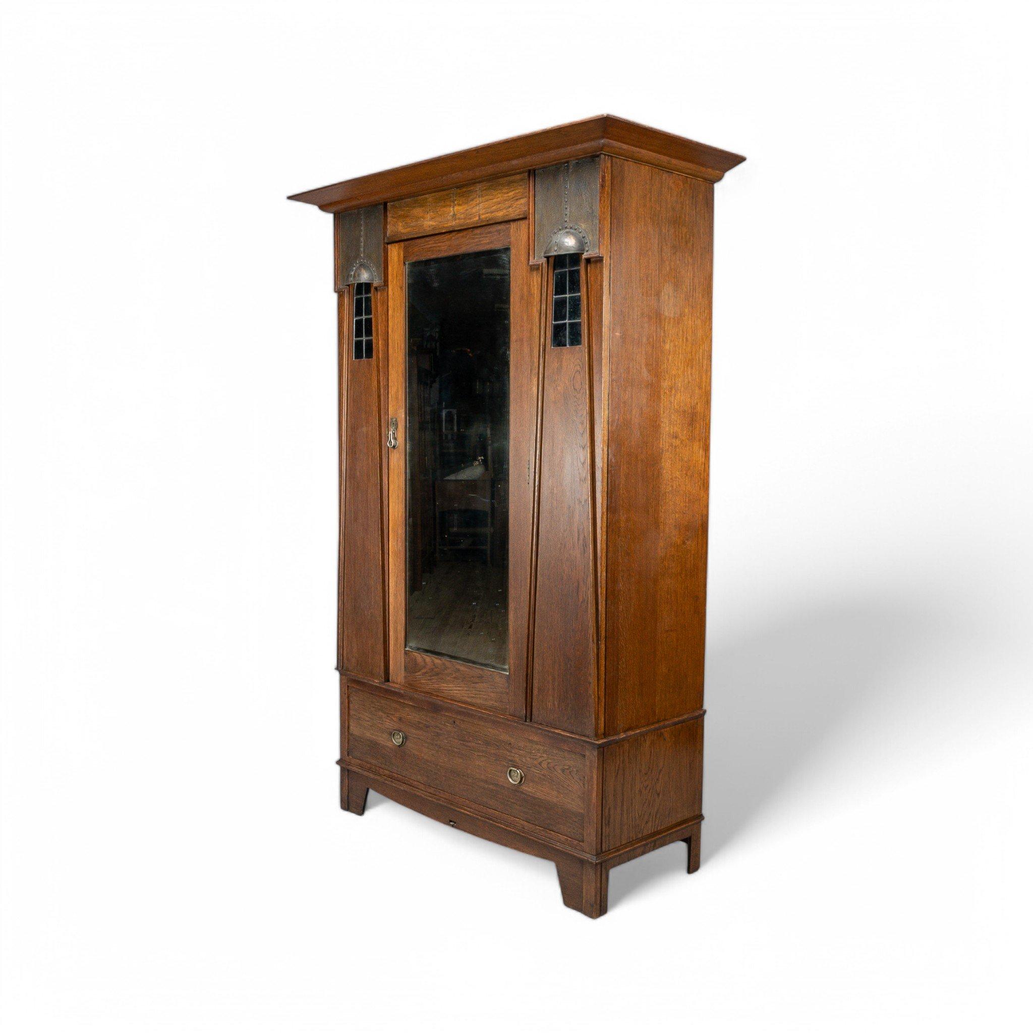 Maple & Co, London
Ein englischer Arts and Crafts Eichenschrank mit ausladendem Gesims, stilisierten dekorativen Kupferhauben über 'A' gerahmten roten Bleiglasleuchten mit einer durchgehenden originalen abgeschrägten Spiegeltür, die sich öffnet, um