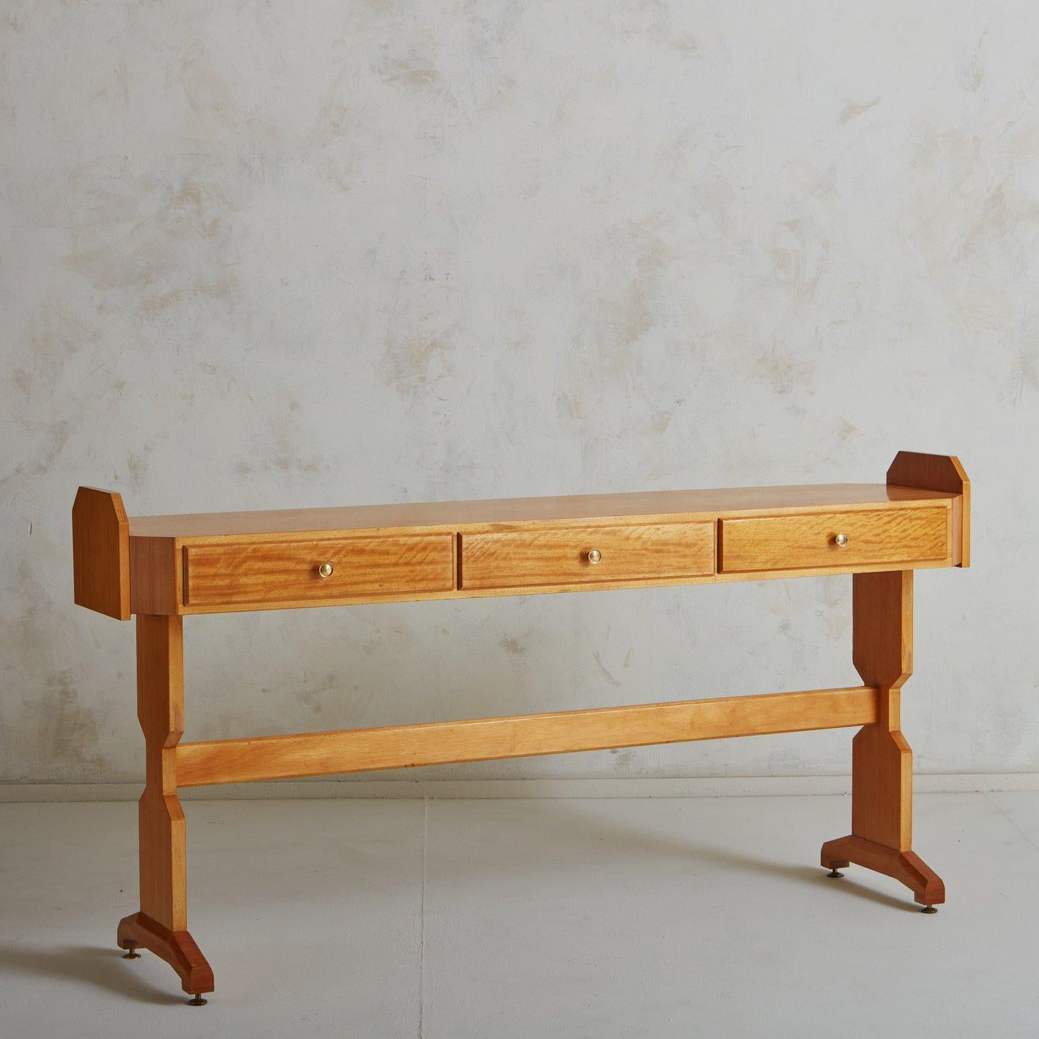 A 1970s Italian console table in the style of Vittorio Dassi. This table was constructed using maple wood with delicate graining. It has a rectangular tabletop with three drawers and circular brass hardware. It stands on sculpturally carved legs