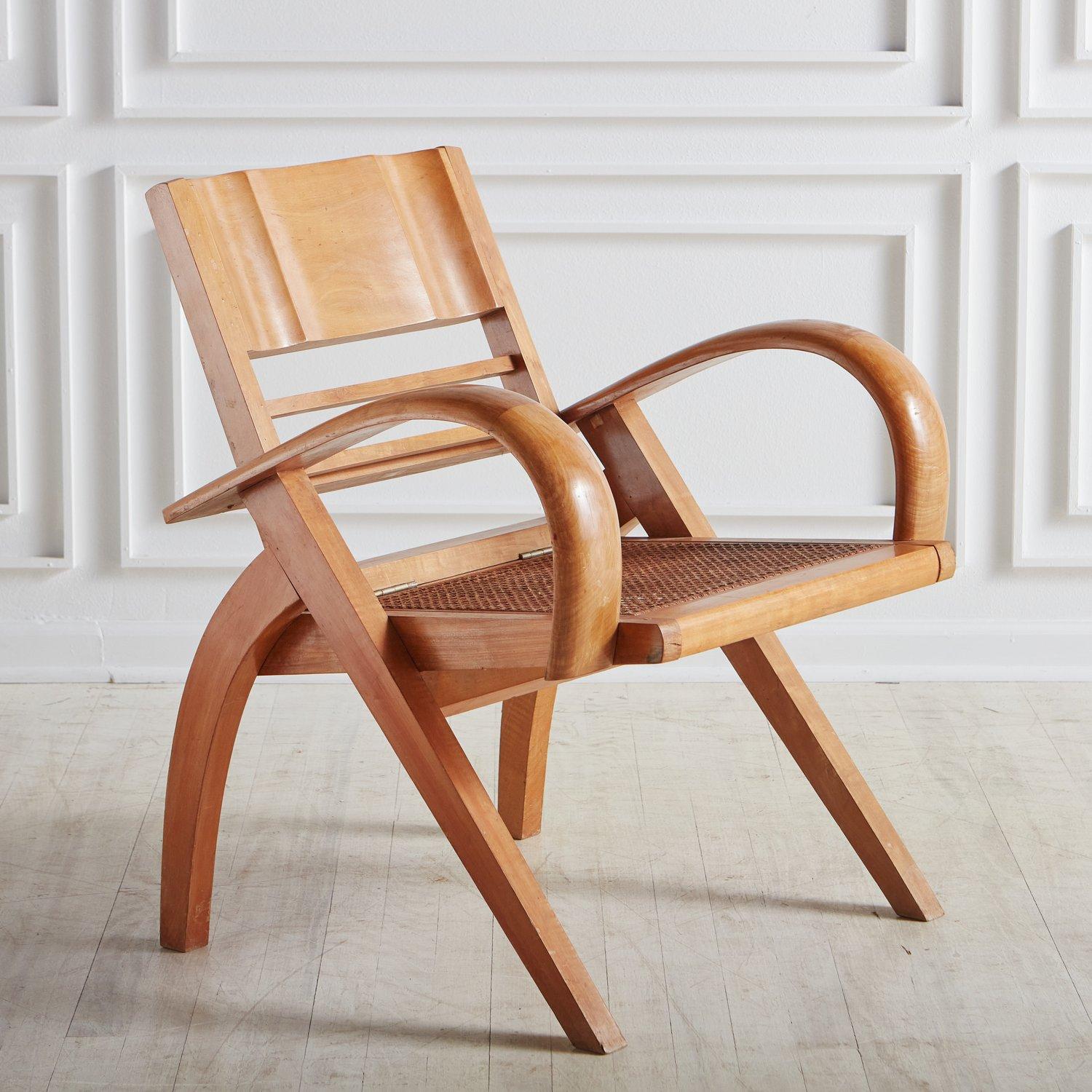 An Art Deco style folding chair sourced in France. This chair has a maple wood frame with elegant curved legs and dramatic bentwood arms. It has a cane seat and the back is on hinges and folds down onto the seat making it compact. This chair