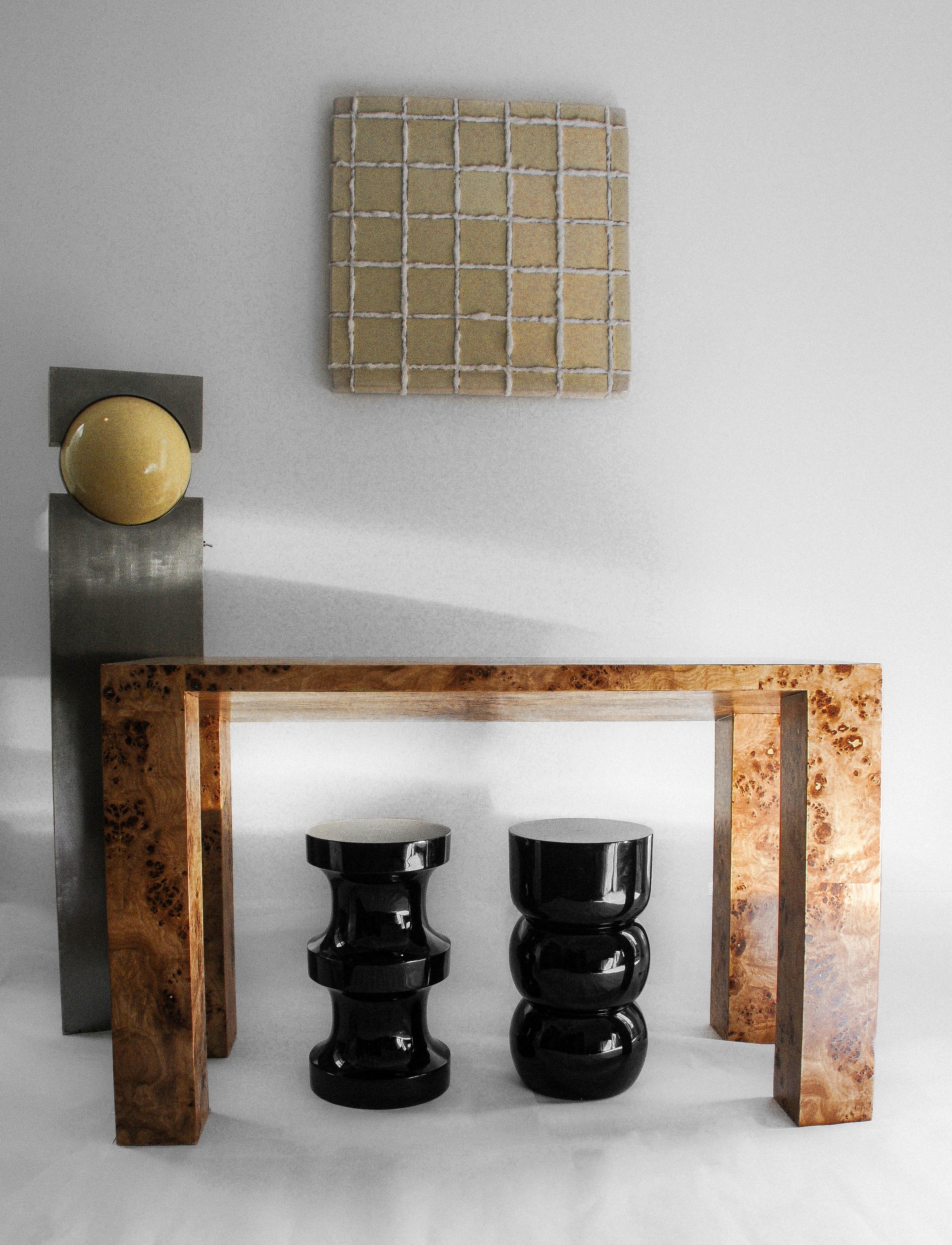 A console table which’s minimalist qualities are clocked by a clasic burl wood veneer. The mappa burl’s patterns grant the object an eccentric elegance while its brutalist structure and asymmetric angled detail seem to subdue its character into a