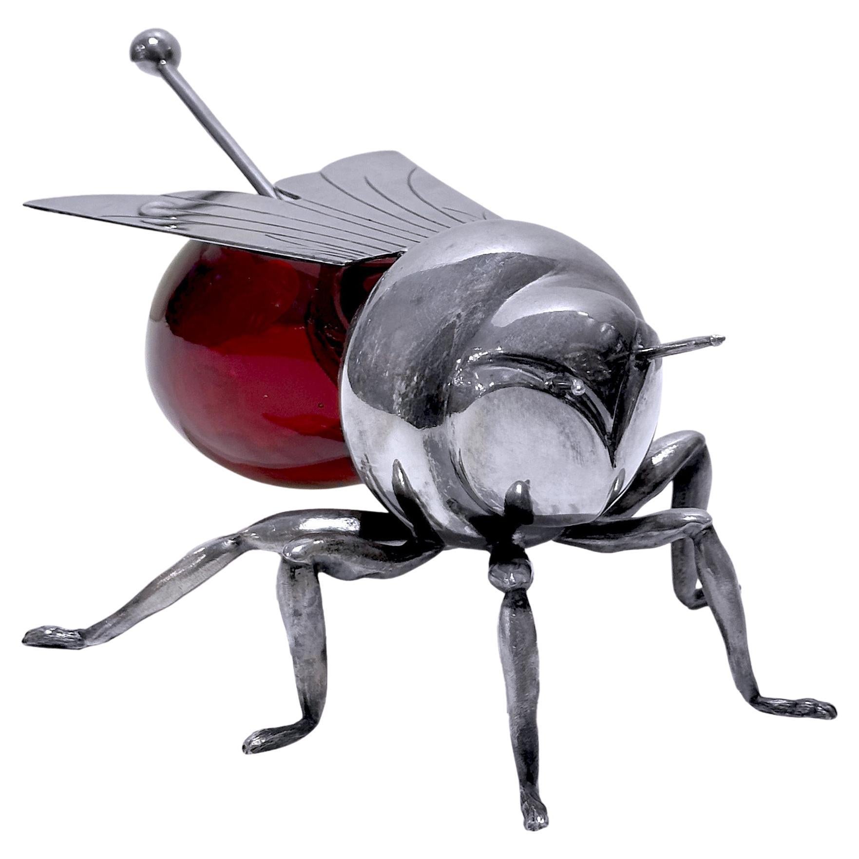 A rare and charming Edwardian-style honey pot in the shape of a bee, crafted in silver plate and ruby red glass by the esteemed English silversmith Mappin & Webb, circa 1960. This whimsical and highly decorative piece features a finely detailed