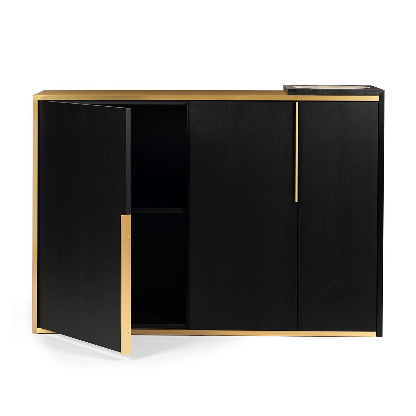 A timeless design of utmost elegance, this cabinet is defined by a rectangular silhouette with an almost seamless aesthetic. Handcrafted of black ash, it is enriched with satin brass details that illuminate it like a splendid glimmer of light. The