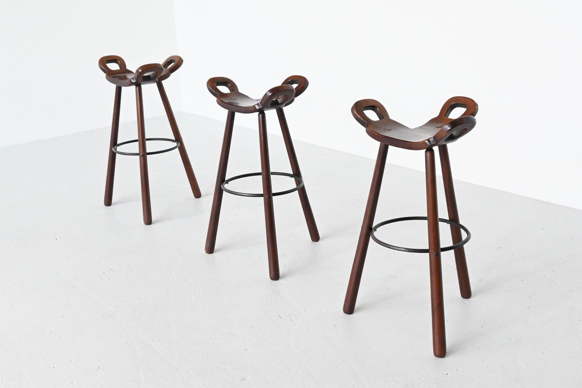 Fantastic set of three Brutalist marbella bar stools manufactured by Confonorm, Spain, 1970. These stools are made of dark stained solid beech wood and they have a solid metal footrest ring to put your feet on and strengthen the construction. The