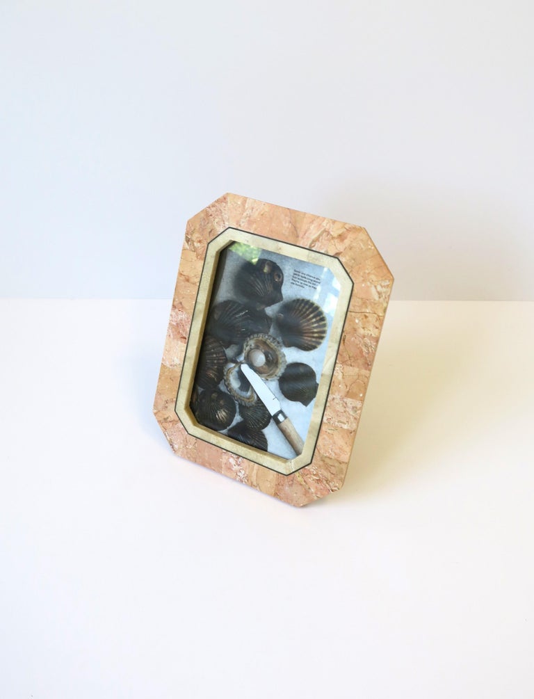 A beautiful '80s marble, stone, and brass picture frame by designer Maitland-Smith, circa late-20th century, 1980s. Marble frame is rectangular/octagonal in shape with marble in peachy pink hues and touches of light beige with thin brass detail