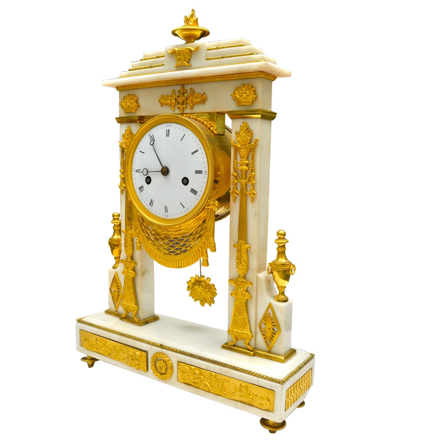A French Empire white marble and gilt bronze portico clock in the form of a triumphal arch; very high quality chased bronze mounts have their original fire gilding. The front pillars are decorated with Roman 'lamp' standards with gilded flames, the