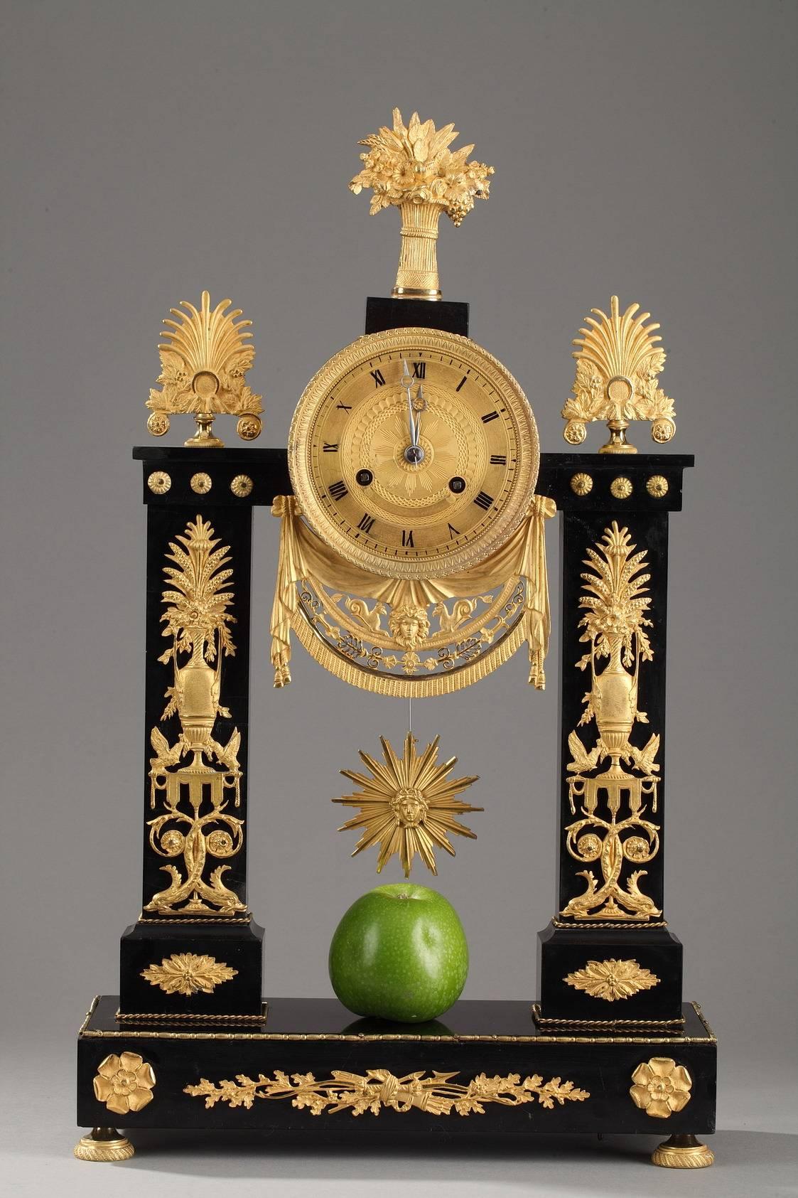 Portico clock in gilt bronze and marble, decorated with flower vases set above canopies, dolphins, and scrollwork. The sculpted, gilt clock face marks the hours in Roman numerals and is bordered with water leaf and small beads. It is set above an