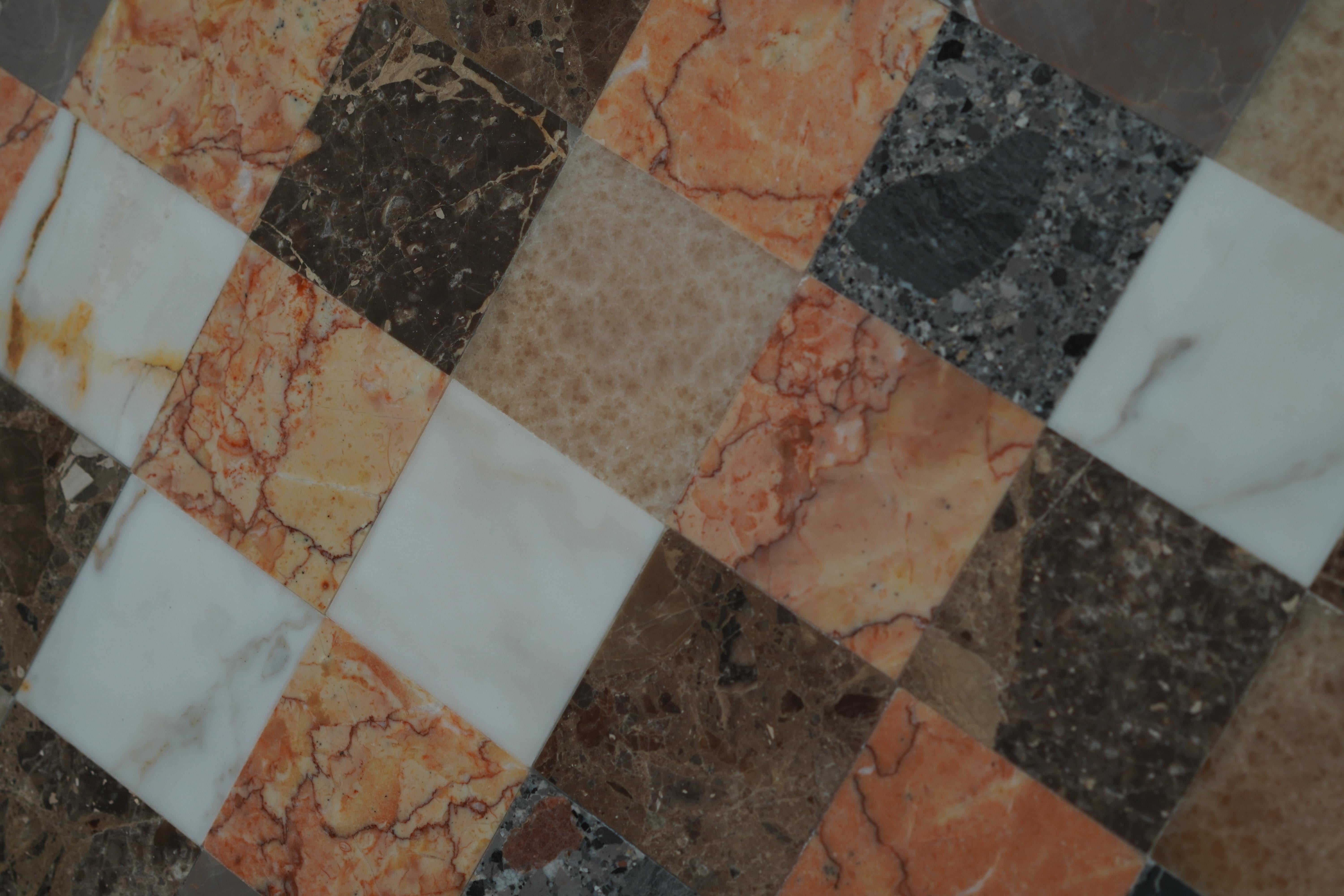 Guéridon en patchwork, fabriqué à Montréal, 2025. Cette table octogonale est faite d'un mélange de marbre et de pierre dans un motif de damier audacieux. Sa base à piédestal et ses tons chauds et neutres en font une pièce remarquable pour tout