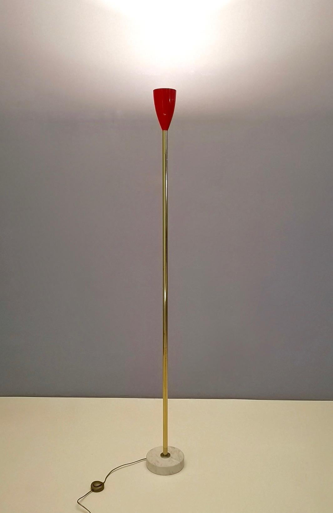 This floor lamp is made in brass, steel, and features a Carrara marble base and a red varnished aluminum lampshade. 
It might show slight traces of use, but it can be considered as in very good original condition and ready to give ambiance to any