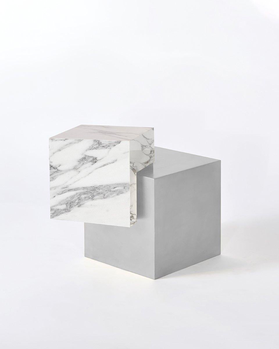 The coexist askew is an exploration of balance, material, and harmony. The materials consist of a stainless steel cube base and a marble cube top. 

The table features a marble cube balanced at an unexpected angle on the brass cube base. The two