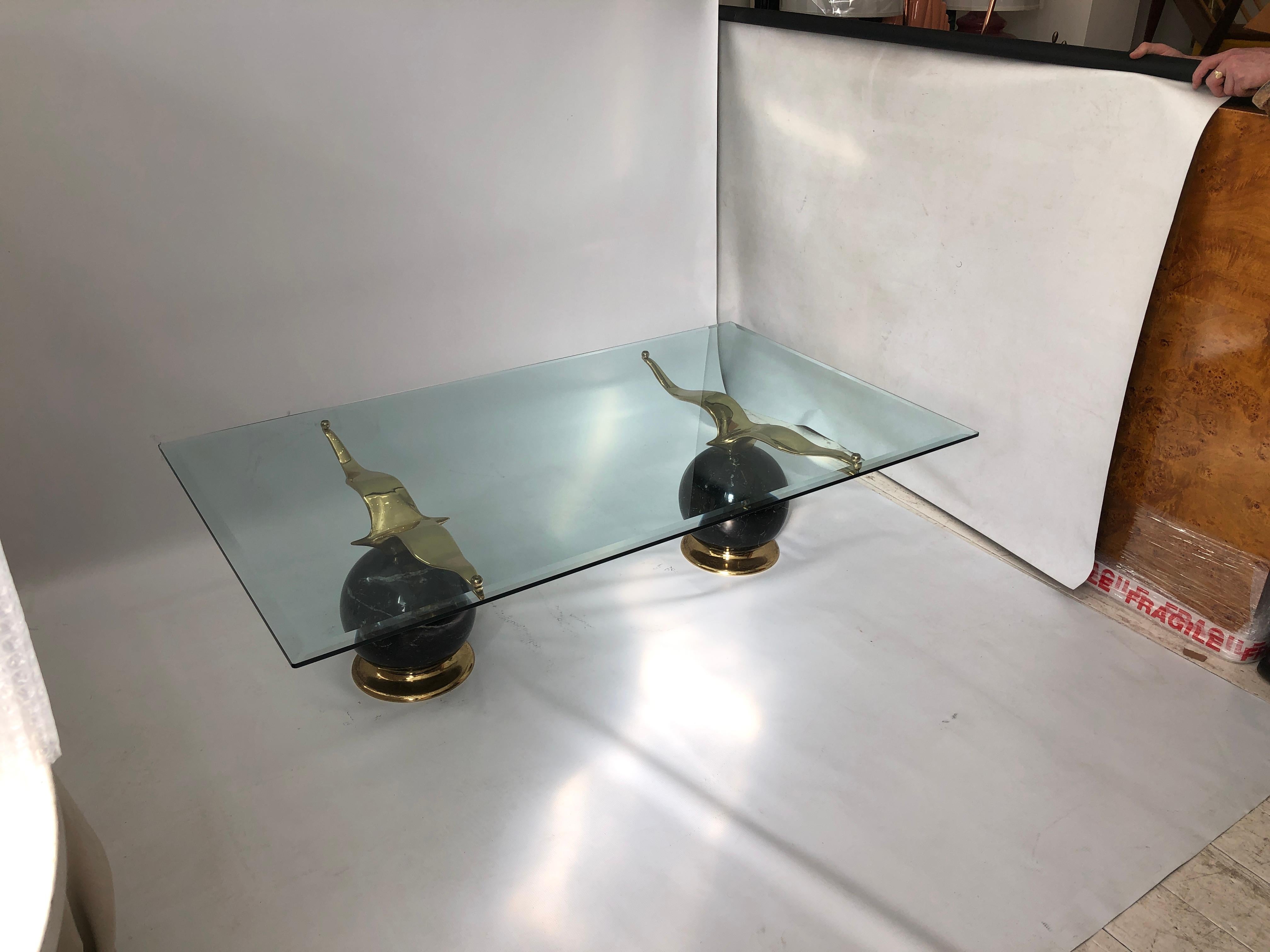 This gorgeous coffee table consists of two solid black marble spheres, atop which sits an elegant brass albatross figure. The two orbs hold a rectangular piece of bevelled glass. 

This piece was imported from a grand Milanese apartment, and exudes