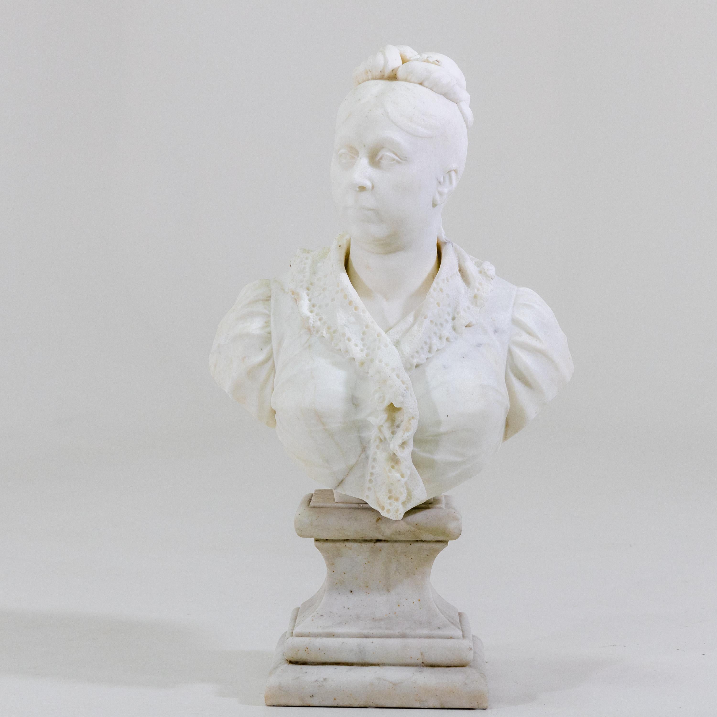 Marble bust of a middle-aged woman with updo and lace-trimmed top standing on a profiled plinth. Her head is slightly turned to the left. Very nice, detailed elaboration.