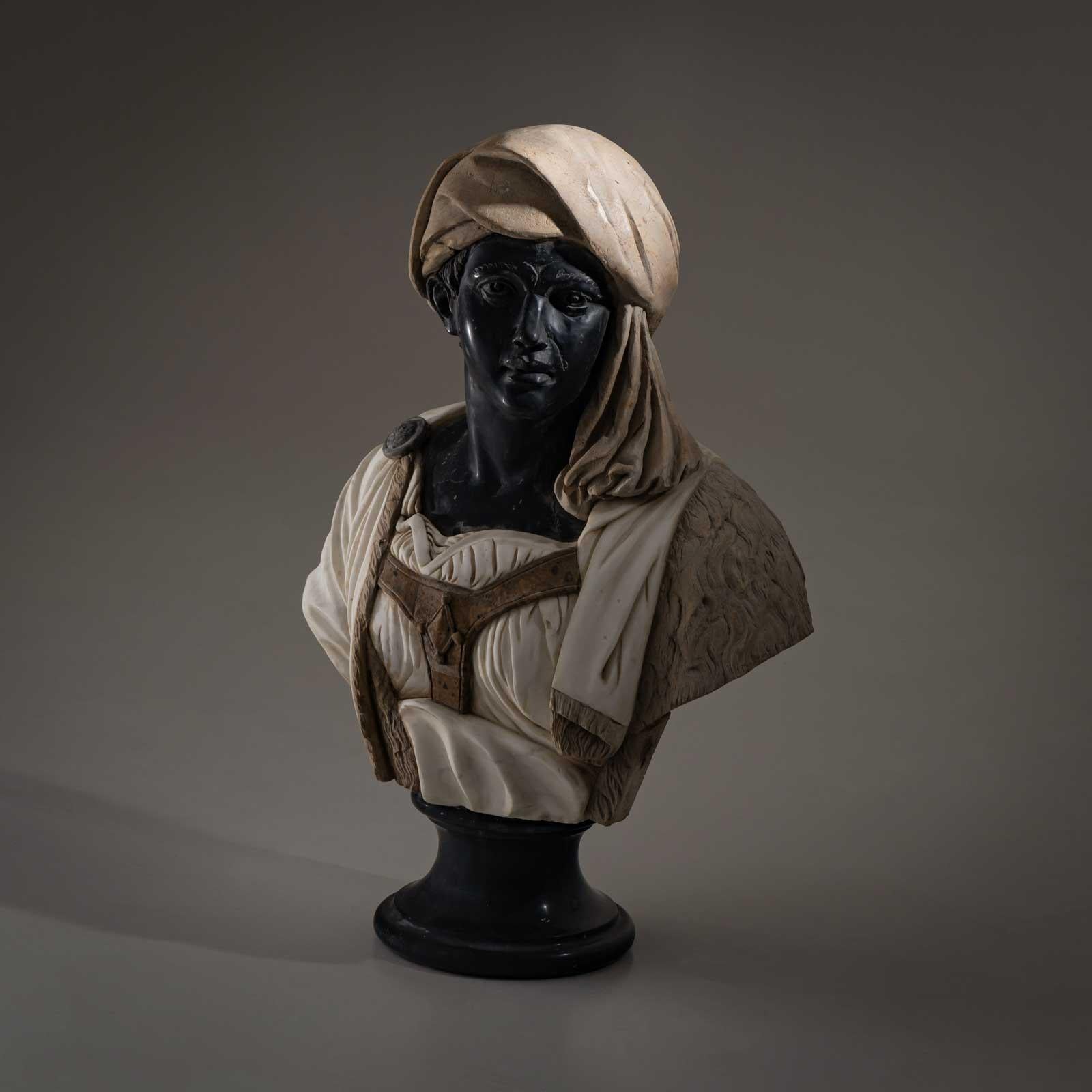 Life-size bust of a dark-skinned man with a headdress and light-coloured clothing. The bust is made of different types of coloured marble and carved by hand. 