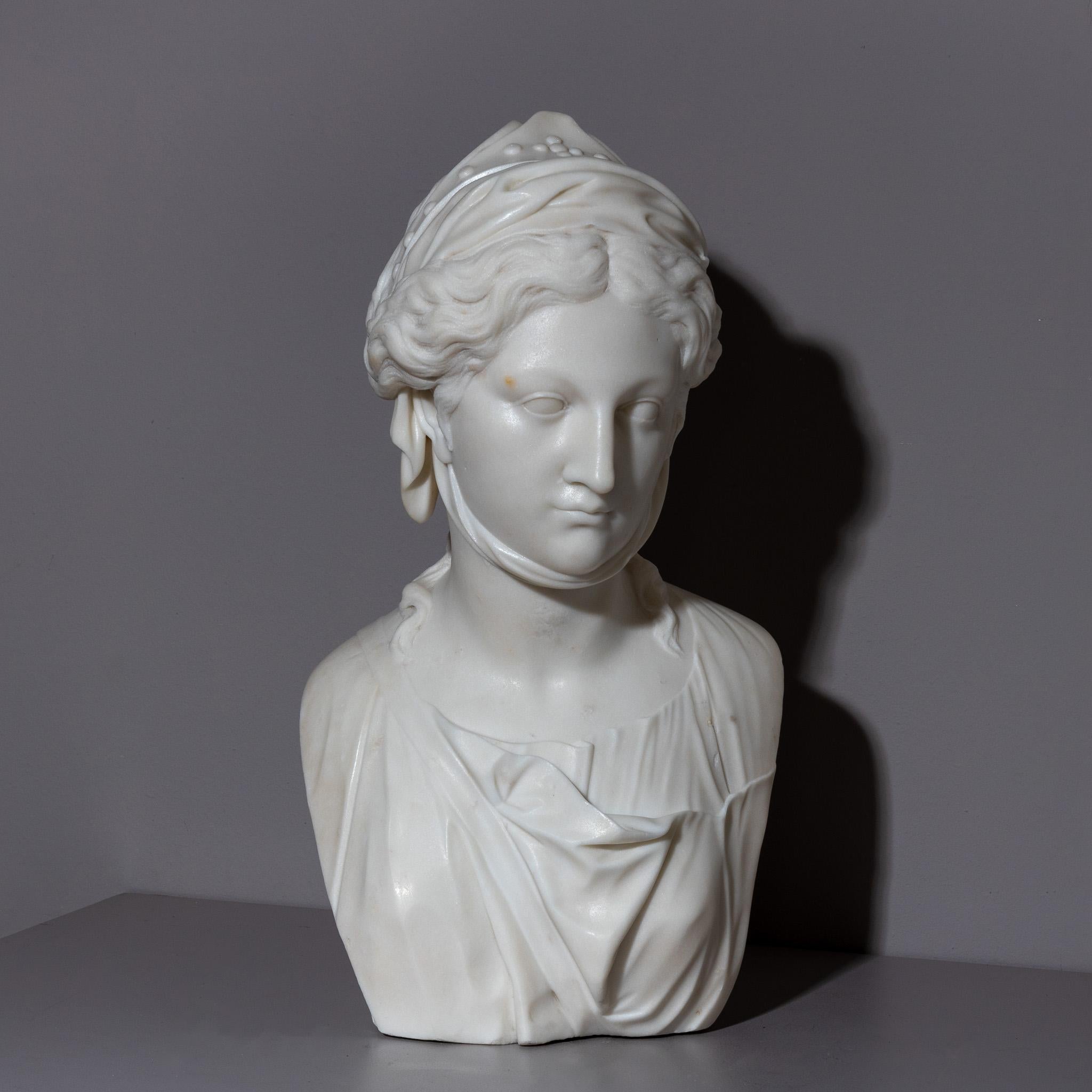Bust of the Zingara or Fortune Teller, finely carved out of marble. The Zingara is depicted with a cloth tied around her chin, which wraps around her elaborately braided hair and ends in a small lace with dot decoration. She is dressed in a draped