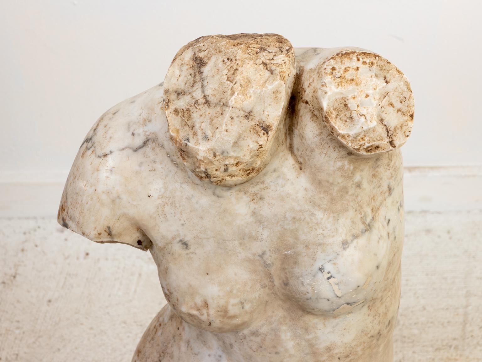 Marble bust of a nude female torso on stand. Please note of wear consistent with age including minor chips, patina, and discoloration to the marble.