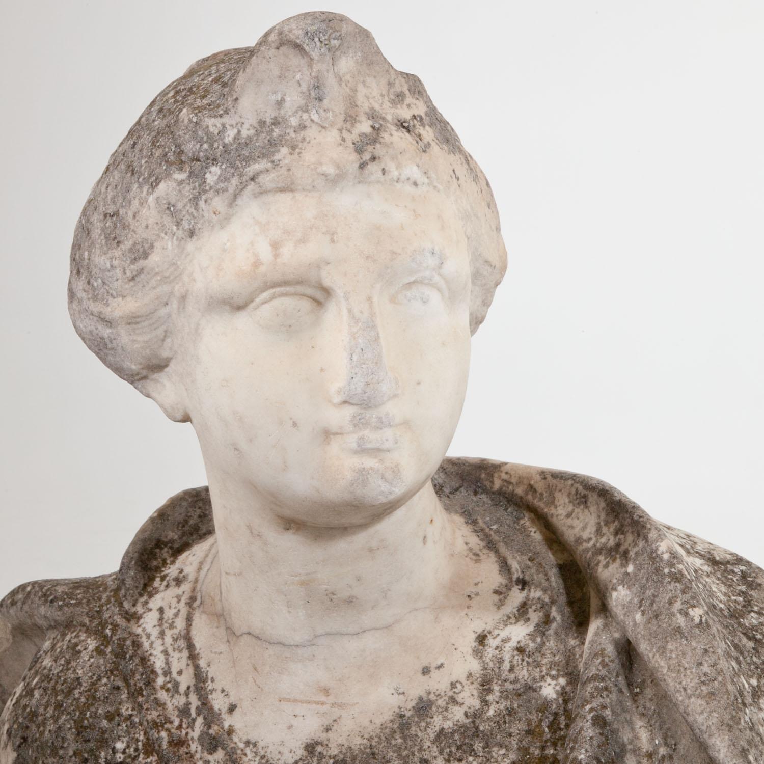 17th century marble bust of a woman wearing a draped gown, her posture is slightly turned to the left. The nose, chin and lips with old abrasions and the gown shows the most natural patina. The backside is concave carved.