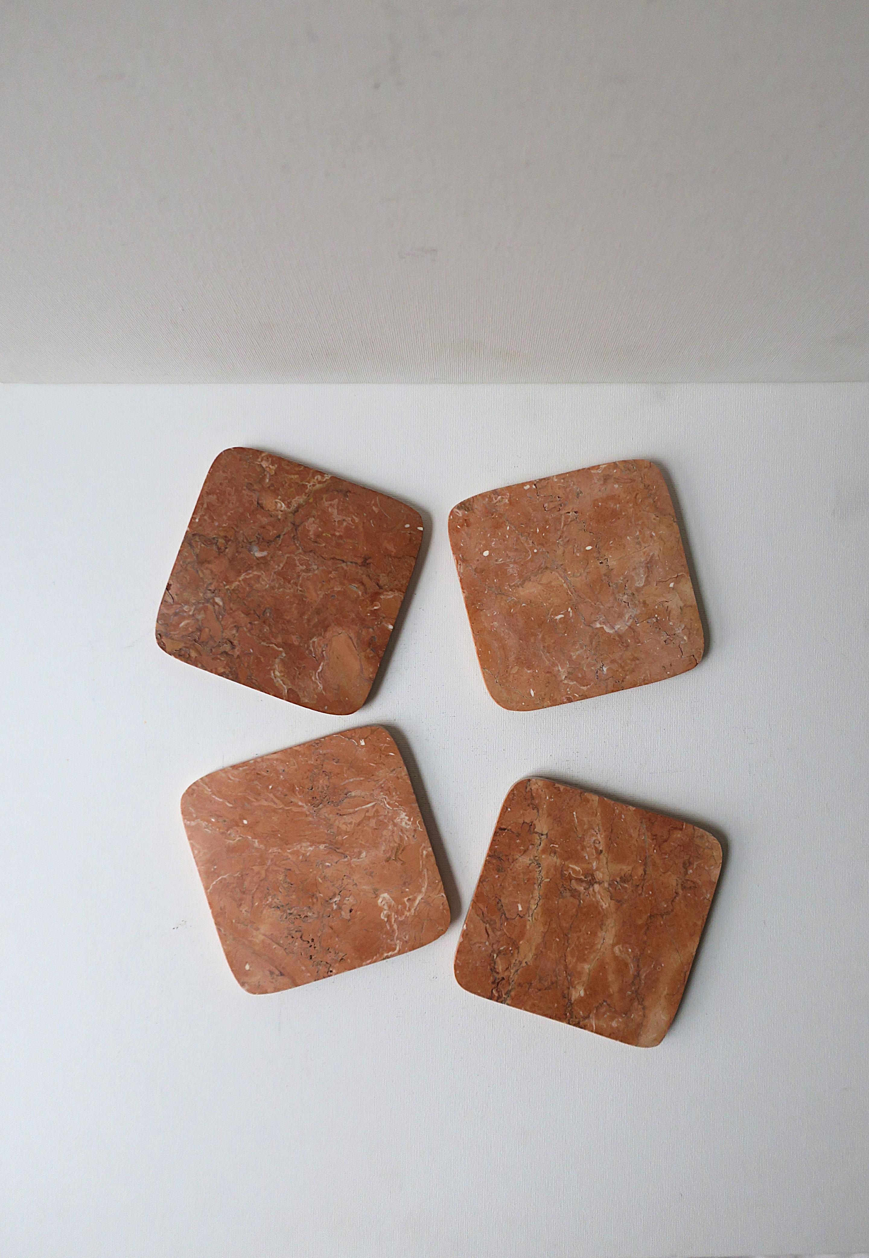 A set of four (4) coral hue marble drinks coasters with cork bottom, Postmodern period, circa late-20th century. Coasters are square with a rounded corner in varying shades of coral marble. A great addition to any bar, bar cart, or entertaining