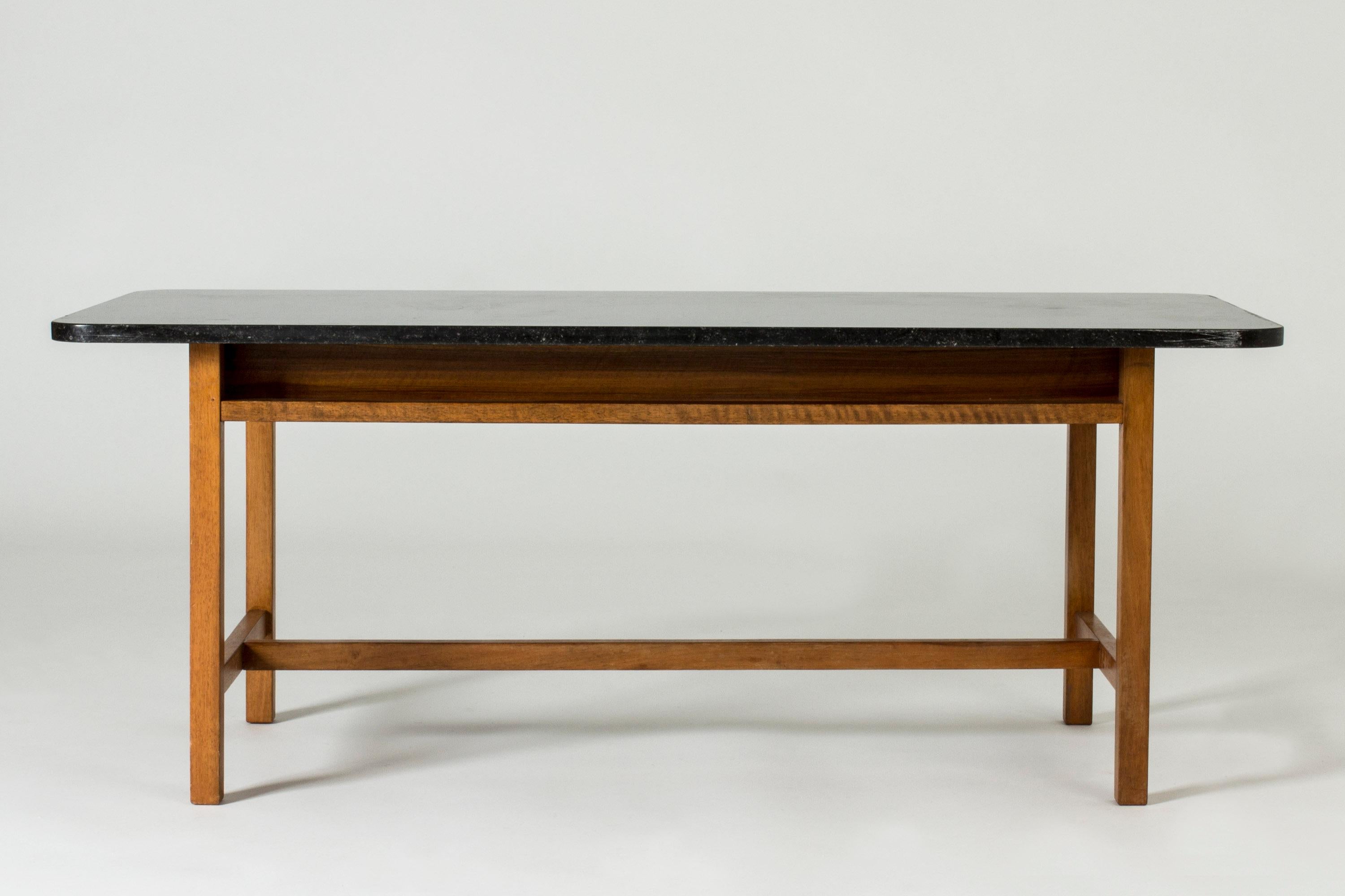 Elegant coffee table by Josef Frank, with a mahogany base and black marble coffee top. Elegant, light base contrasts with the heavy top. Rounded corners.