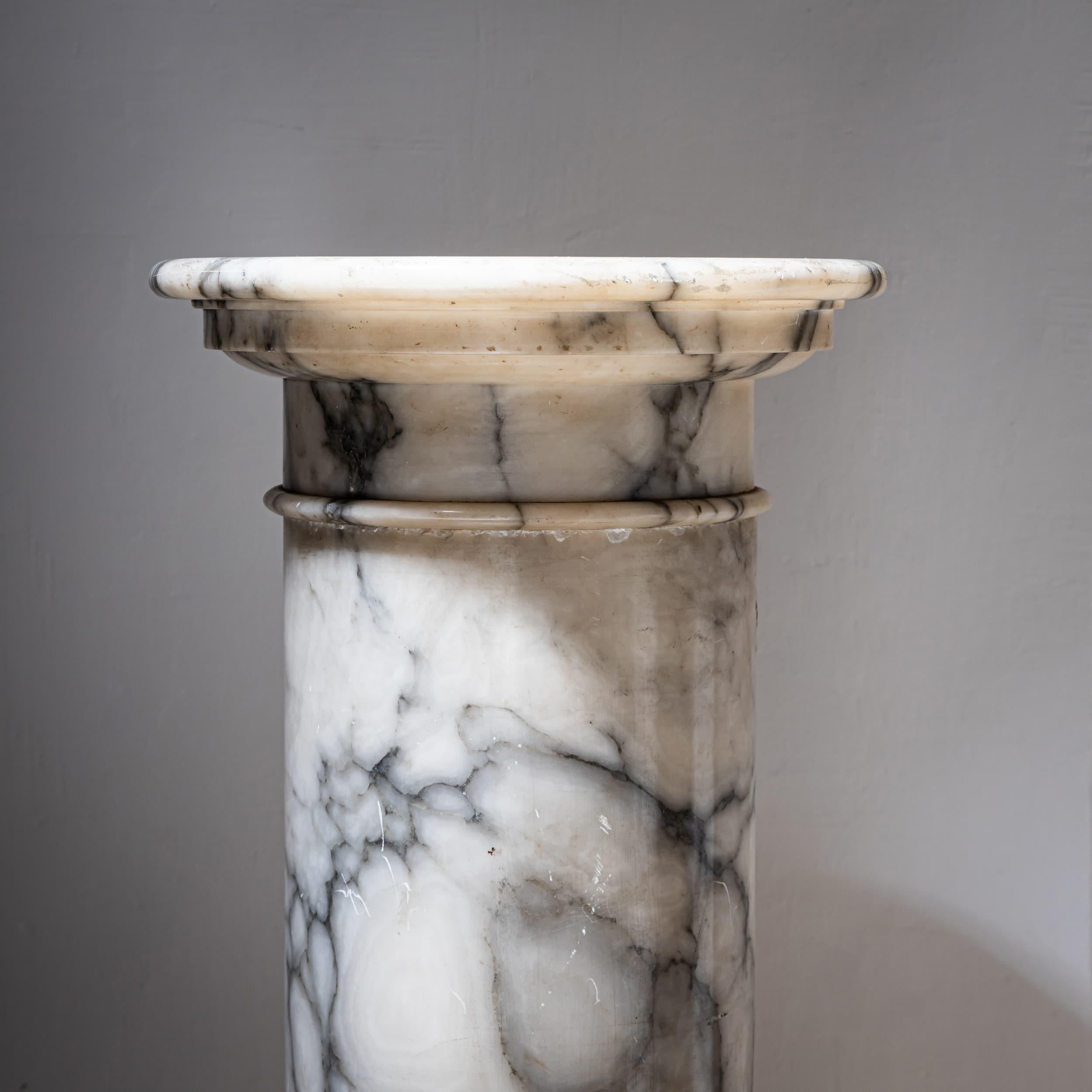 Columna de mármol blanco con vetas grises. El eje liso está dividido por tres sutiles molduras anulares. Apoyada sobre una base octogonal, esta columna es ideal como pedestal para esculturas o bustos.