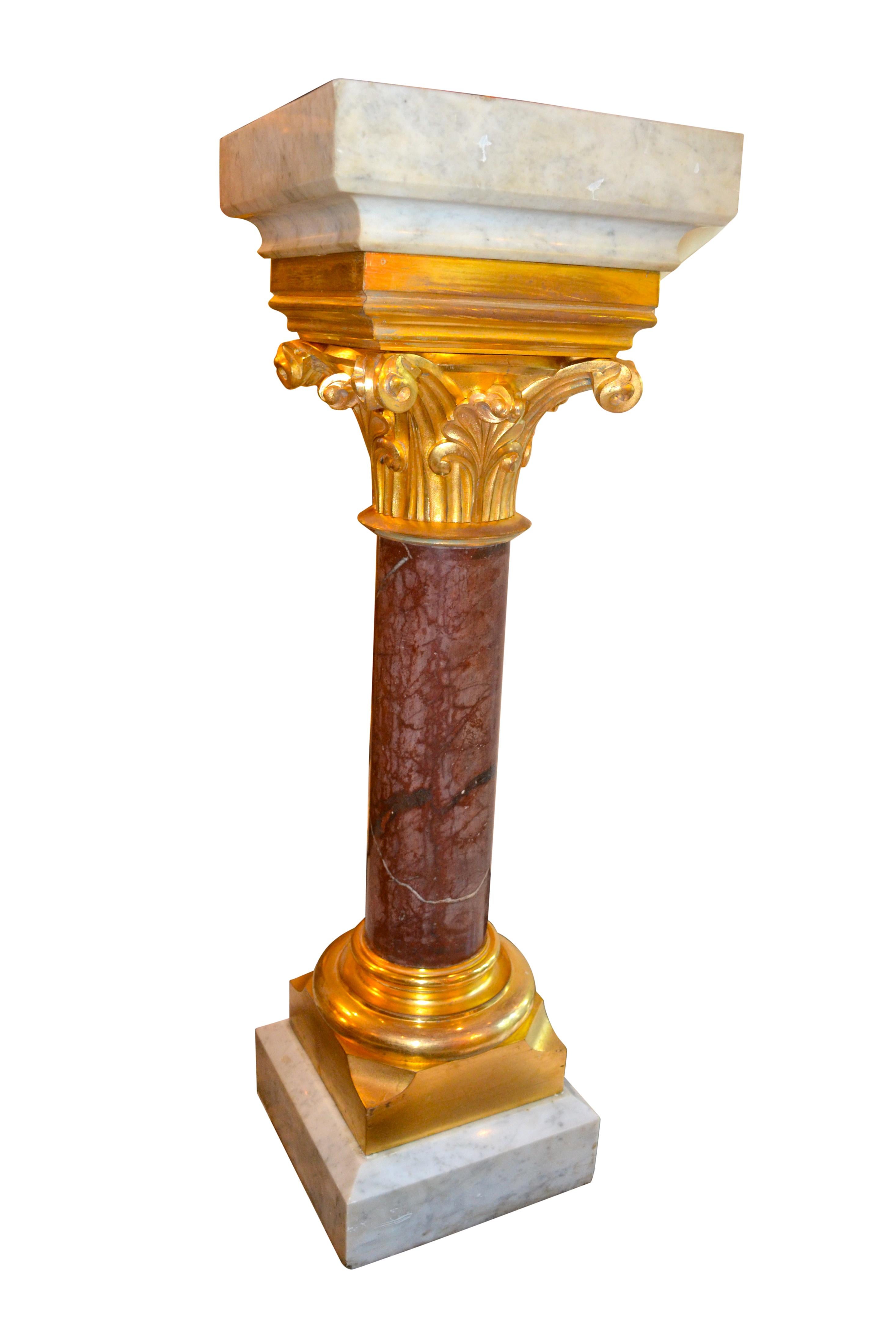 A dark red/brown circular marble column with a large gilded bronze Corinthian capital and a \r gilded bronze 