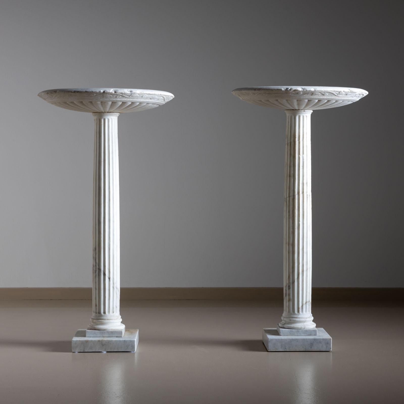 Pair of marble pedestals on square plinths. The pedestals stand on classic bases with fluted shafts and end in shallow bowls with gadrooned walls and decorative relief in the form of leafy tendrils. The plinths had been added later. 