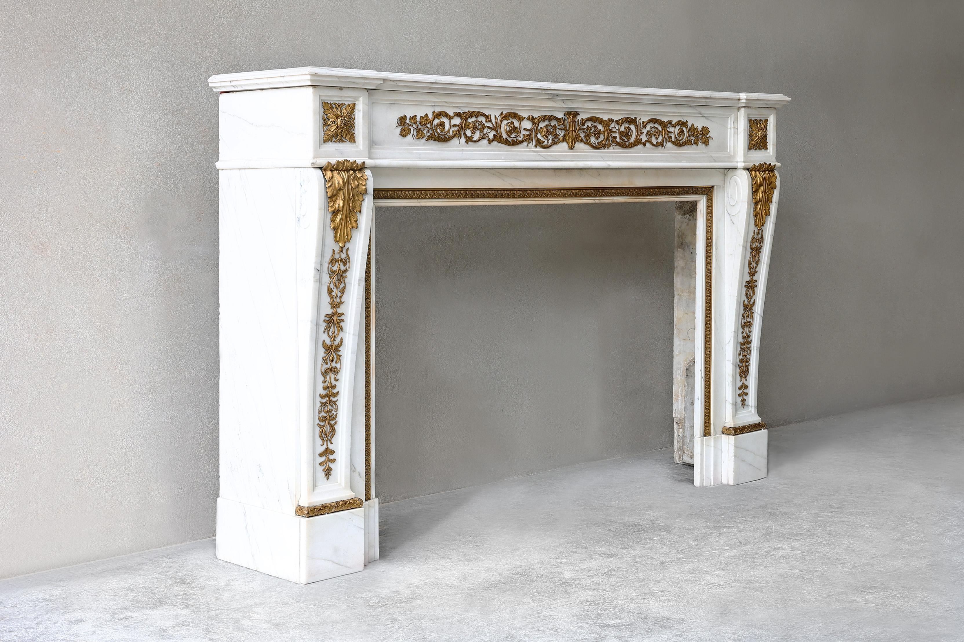 Very chic antique fireplace of Carrara marble with gilded gold. An elegant fireplace with beautiful ornaments and decorations in gilded gold in the front part and continuing on the legs. This 19th century fireplace is in the style of Louis XVI and