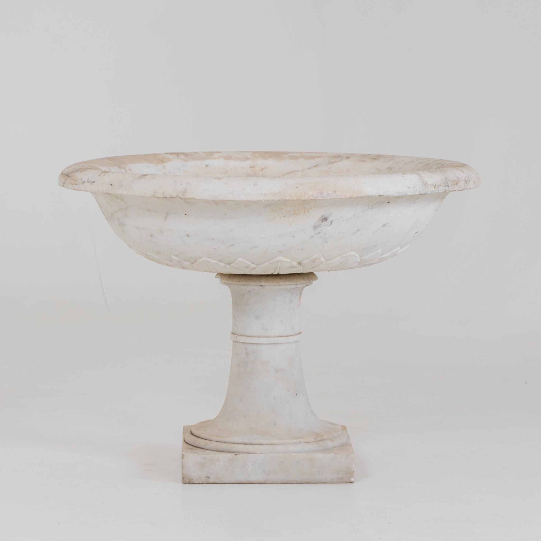 Round marble fountain basin on conical shaft and square plinth and discreet leaf frieze on the tulip-shaped wall.