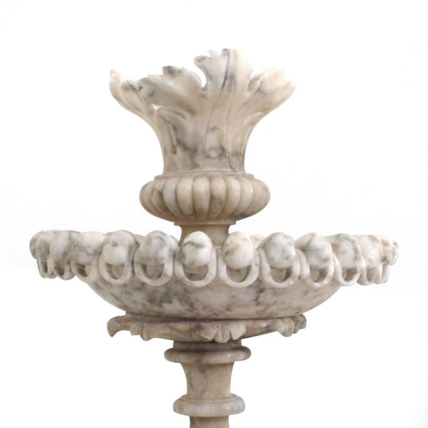 Three-tier marble table fountain of the 19th century on an elegant, profiled base. Each tier shows stylized leaves and is boarderd by ball ornaments with bows underneath.