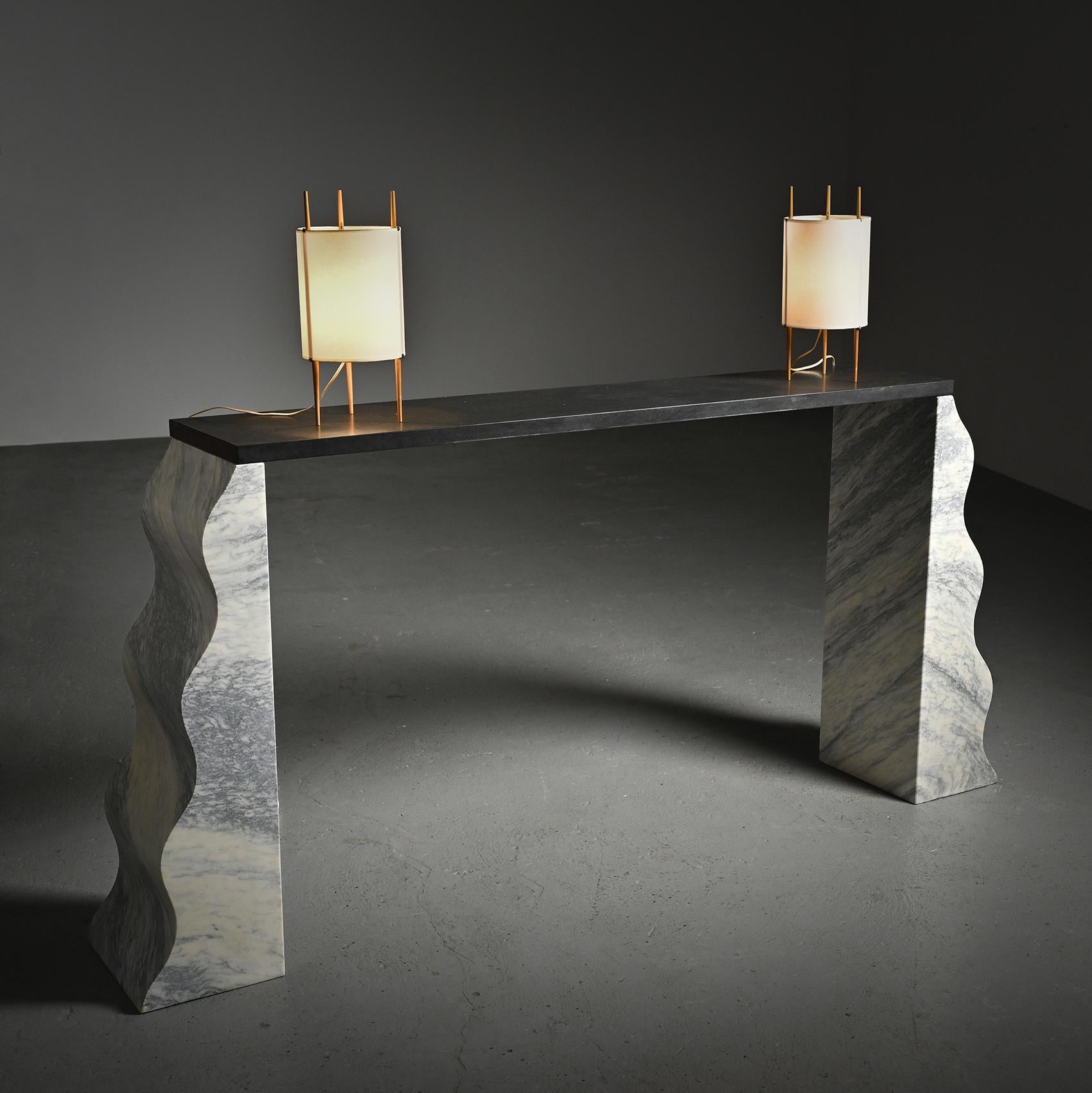 form.

Comprising two white marble pedestals intricately veined in grey, sculpted with a graceful wave-like design, it elegantly upholds a rectangular Zimbabwe's black granit.

Manufacturer : Ultima Edizione, 1987.