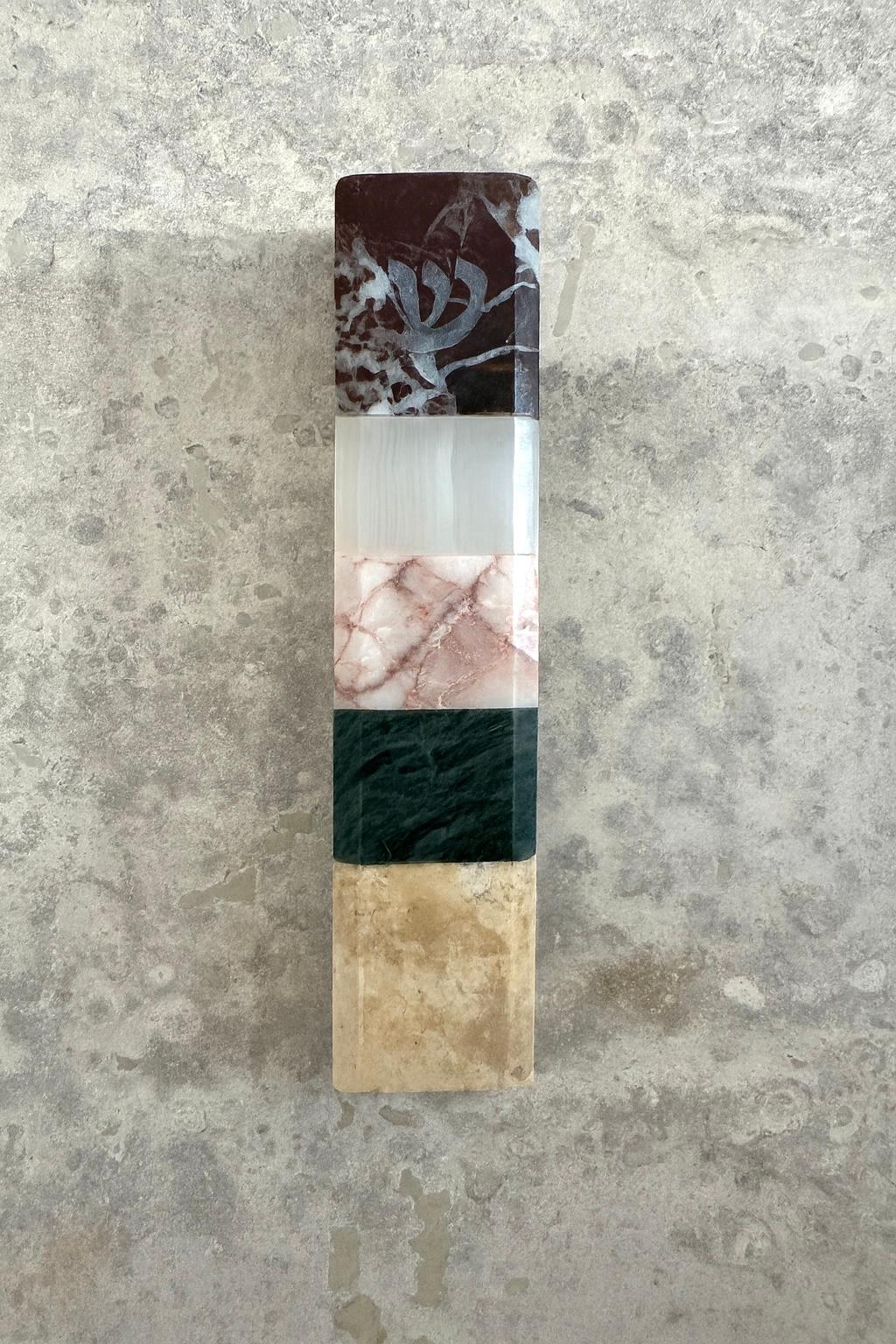 Esta Mezuzah contemporánea de Studio Gaïa transforma un objeto sagrado en una pieza de diseño coleccionable, un encuentro entre la tradición y la escultura moderna.

Tallada a mano en mármol Rosso Levanto, ónice blanco, mármol rosa, mármol verde y