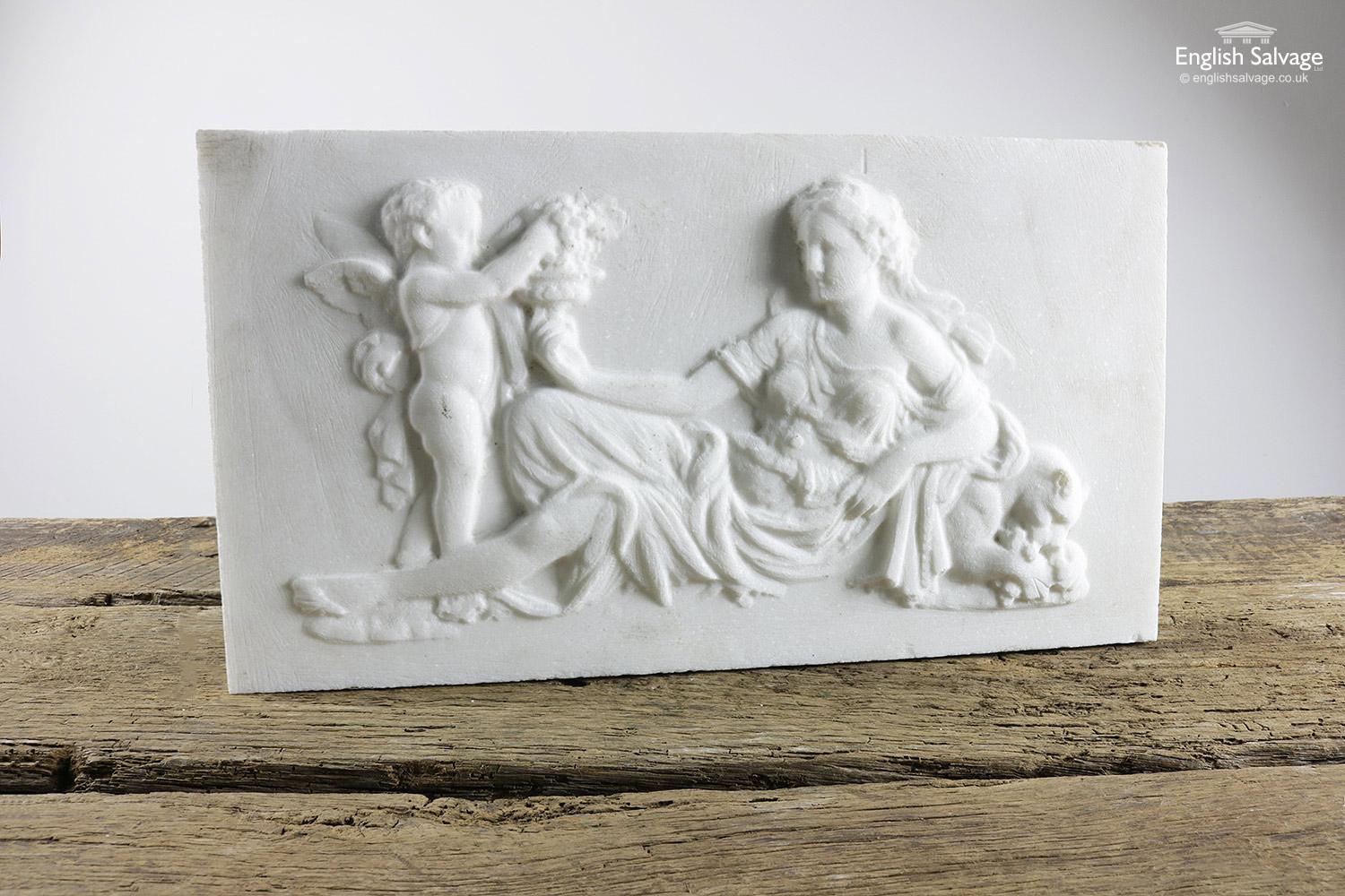 White marble plaque depicting a putto being handed grapes by Cybele, the earth goddess, who is supported by a lion. The overall depth including the carving is 4.8cm. There are some very small nibbles to the edges of the plaque and a few small