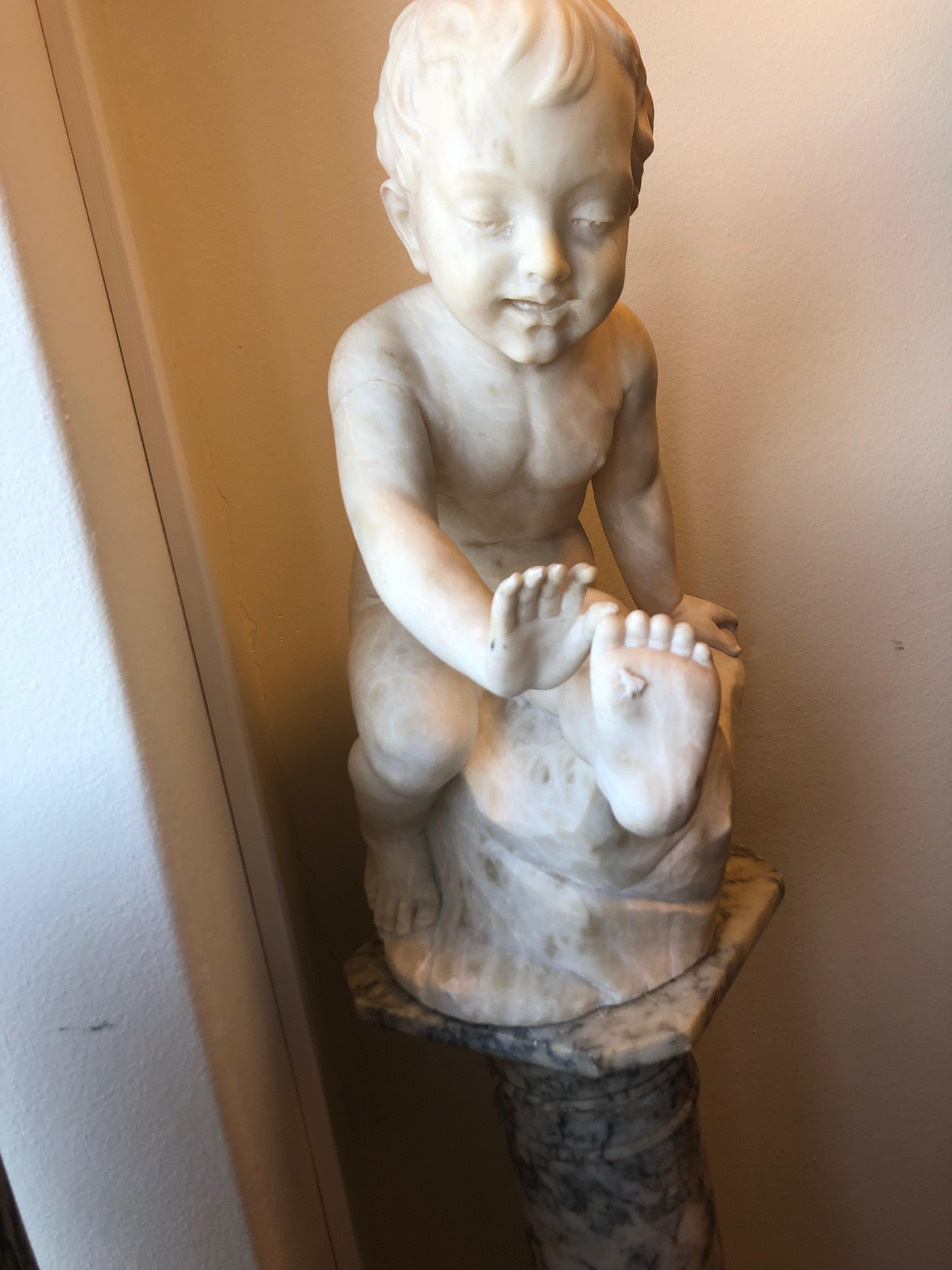 An amazing model depicting a sitting boy trying to catch a bee on his foot. Sculptured of marble and coming with its original pedestal also made of marble.