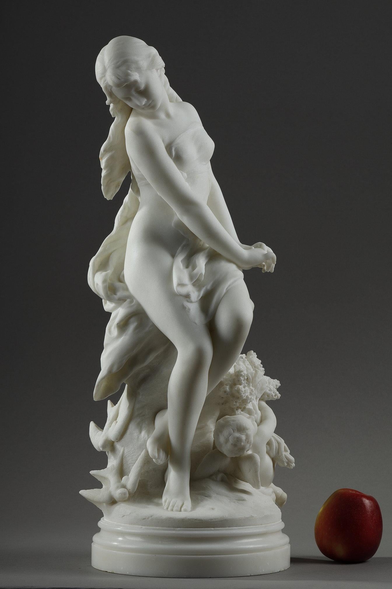 Élégante sculpture en marbre de Carrare représentant Vénus (Aphrodite) portant un voile léger, assise sur un rocher avec Cupidon (Eros) à ses pieds, portant un grand bouquet de fleurs et entourée d'hirondelles. Ce groupe en marbre est une allégorie