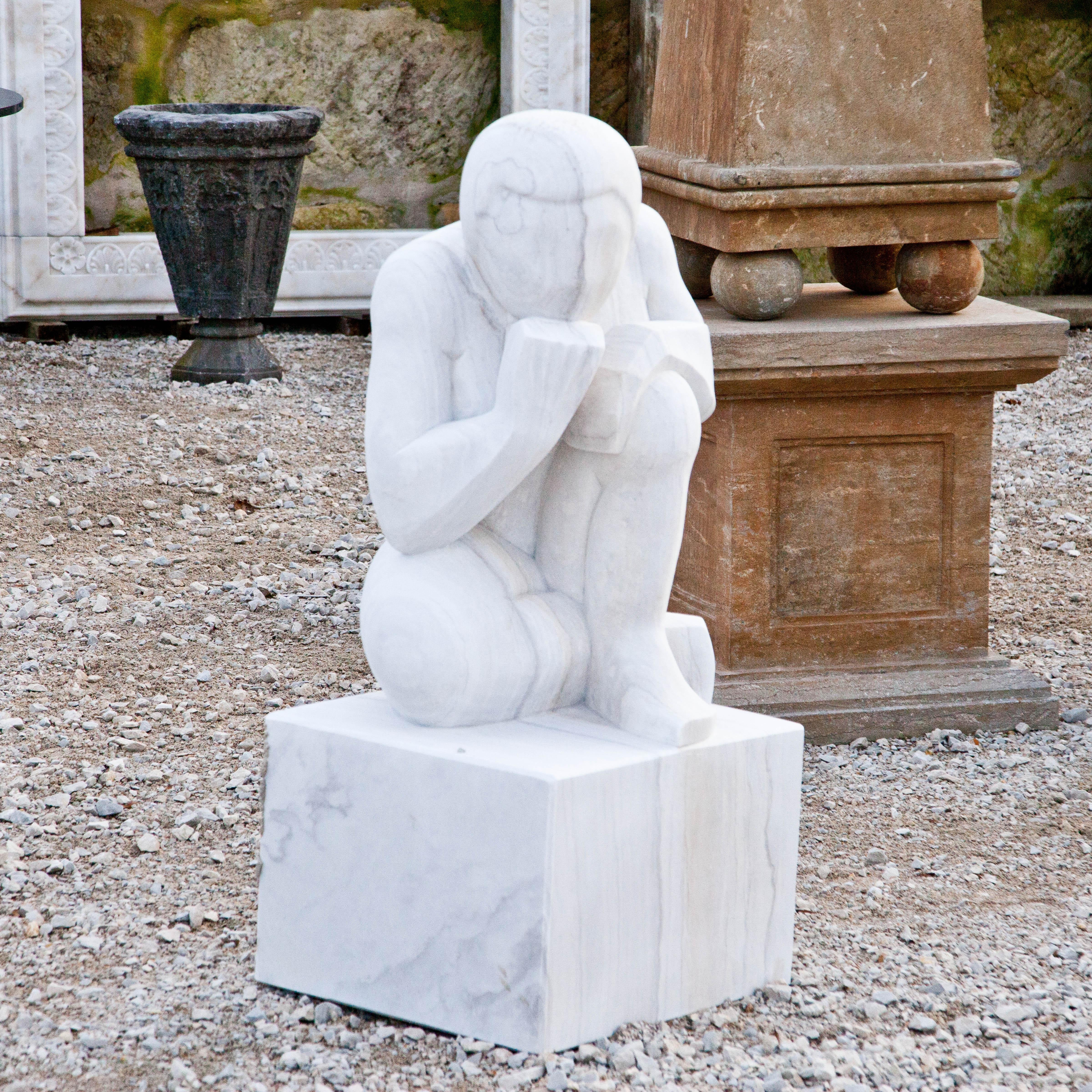 An abstract figure of a thinker squatting on a square pedestal, his chin resting on his fist. The sculpture is handcrafted from marble and has a fine surface structure.